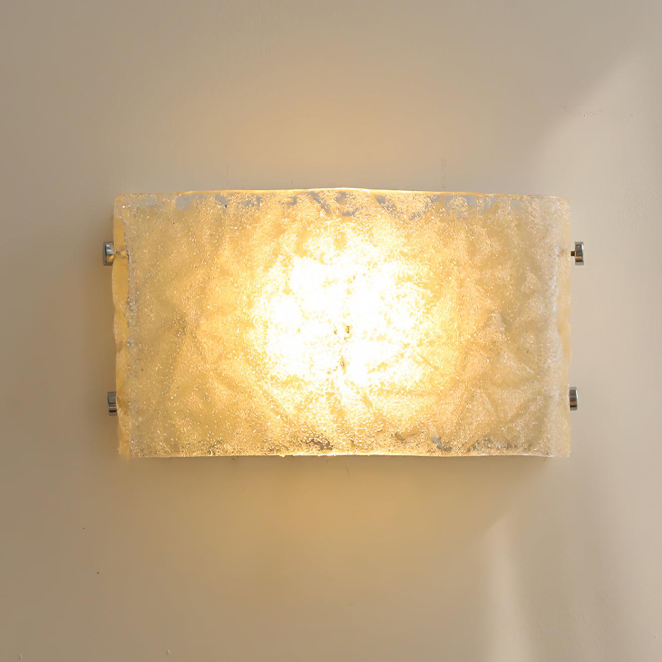 Front view of illuminated curved textured glass wall light with a bright warm-looking centre and chrome fasteners