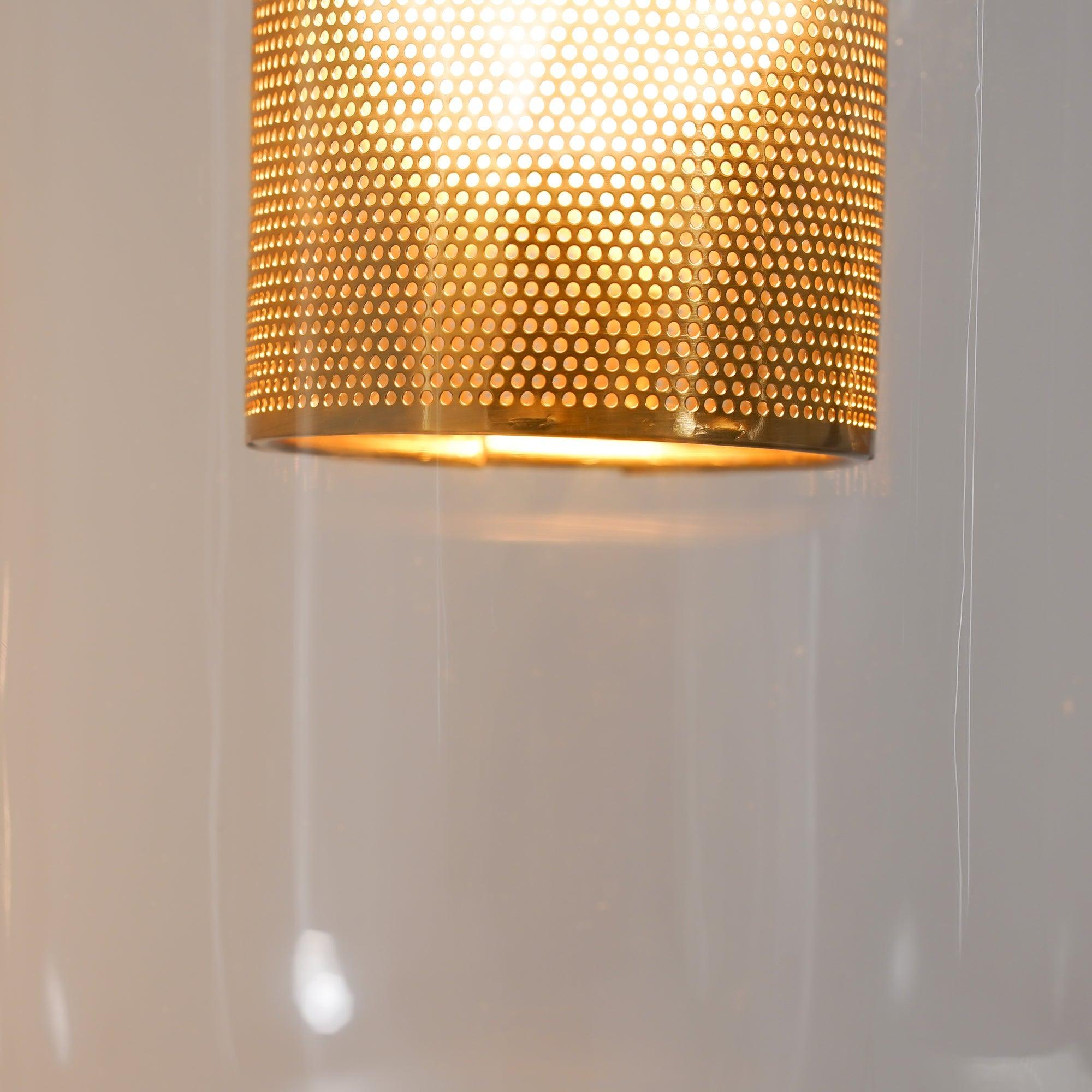 Macro detail of the glowing lower rim of Vadim perforated metal cylinder behind smooth clear glass