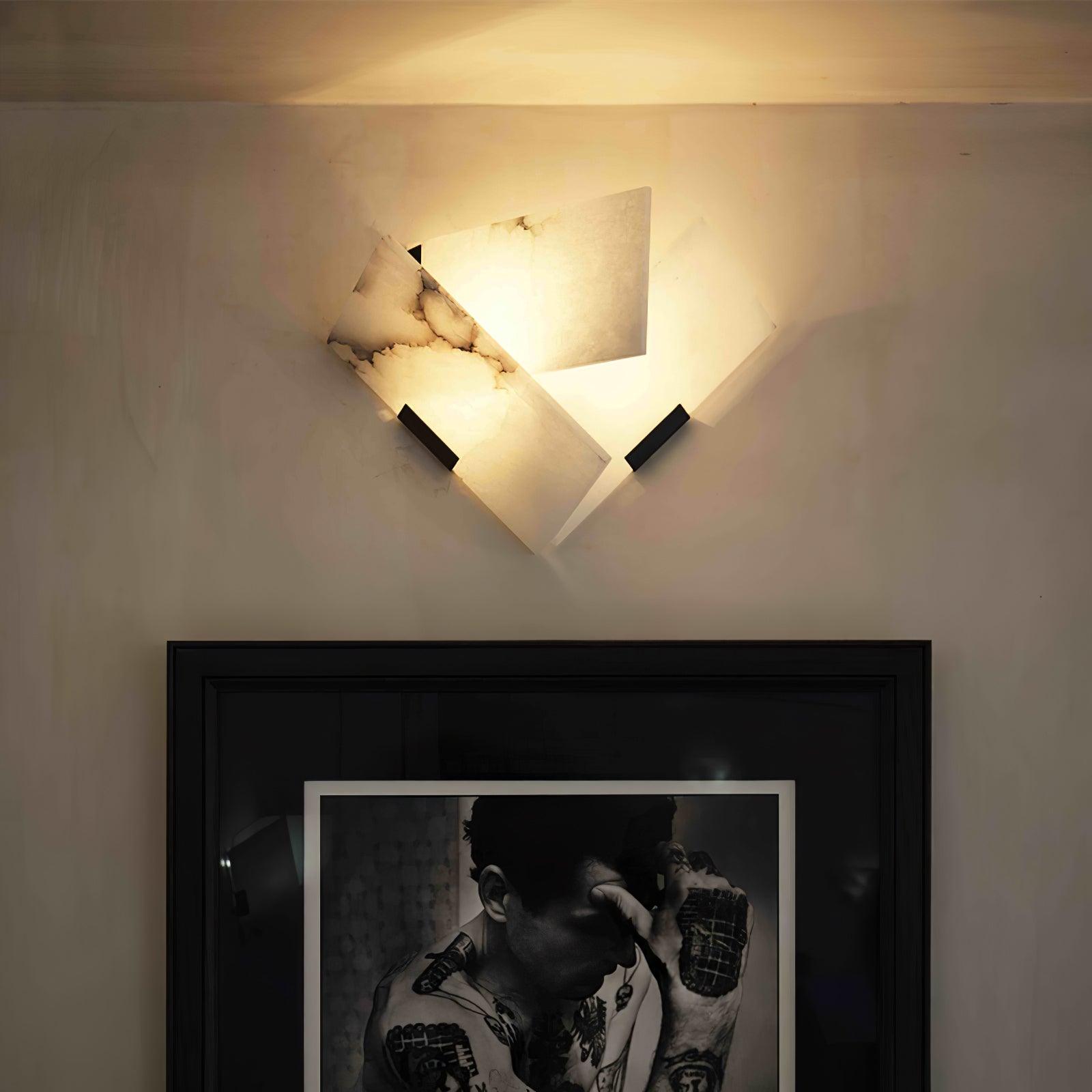 Lit angular alabaster wall sconce with dark veins and black clips above a framed portrait