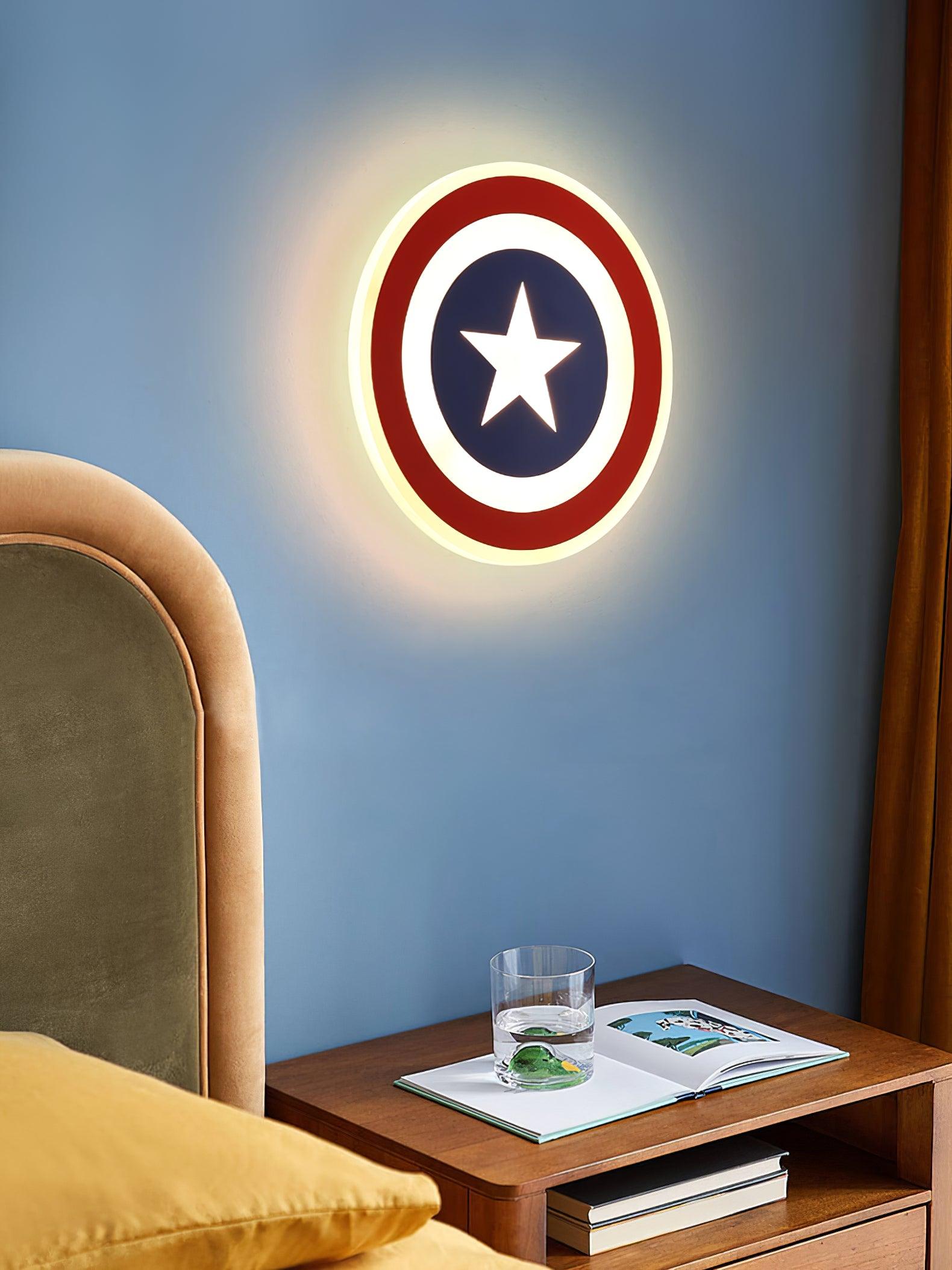 Red-ring star lamp on blue wall above wooden nightstand with glass and book, beside yellow cushion
