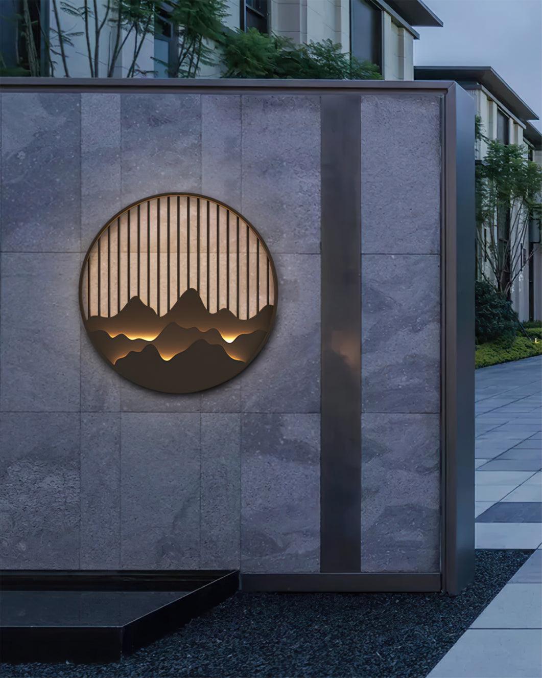 Large mountain landscape light on grey tiled exterior wall beside dark vertical trim and paved garden path