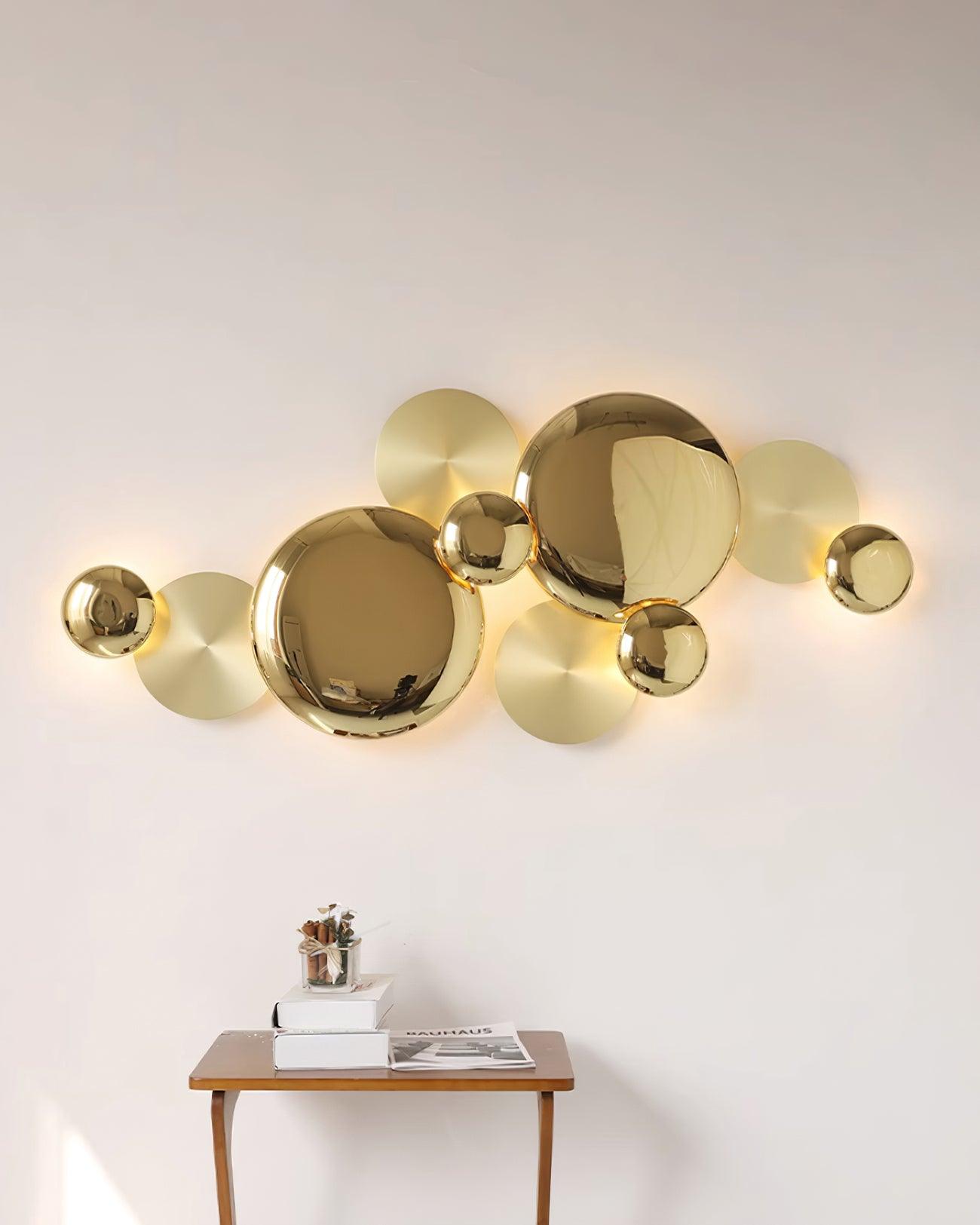 Wider view of the illuminated gold disc wall lamp above a wood console with stacked books