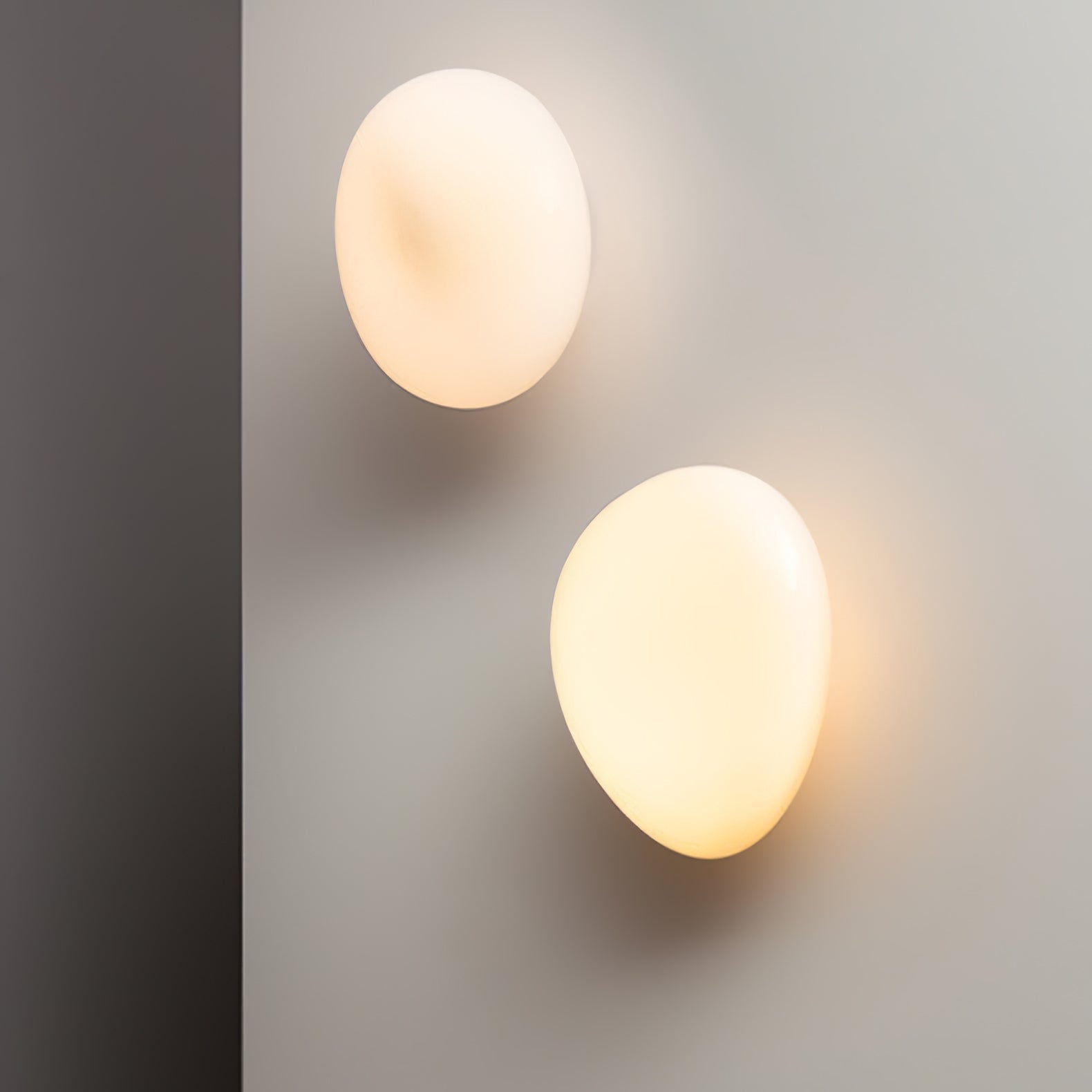 Two illuminated white oval glass wall lights beside a gray inside wall corner