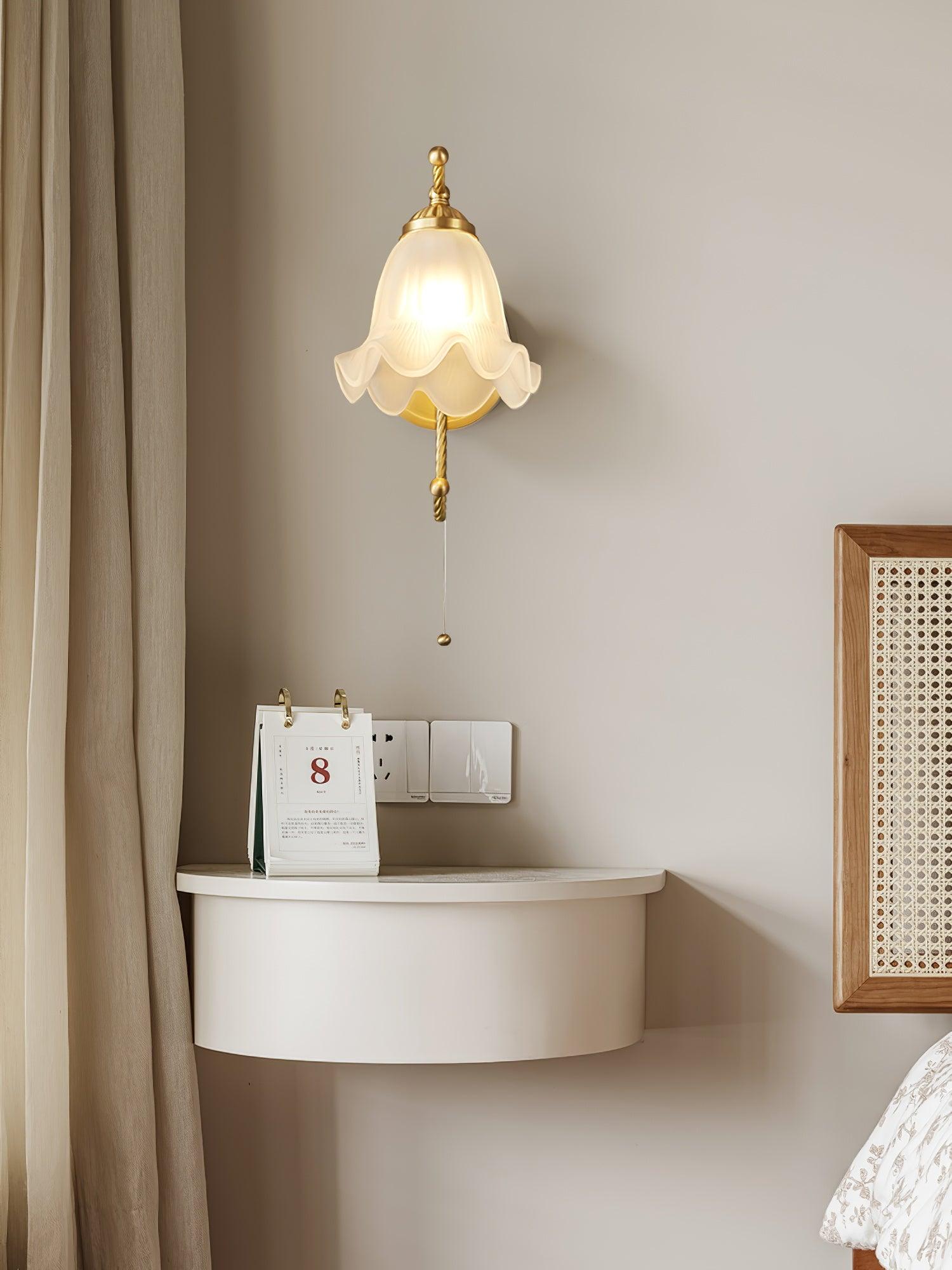 Front lit scalloped glass lamp above curved white bedside cabinet and calendar, beside curtain and woven headboard