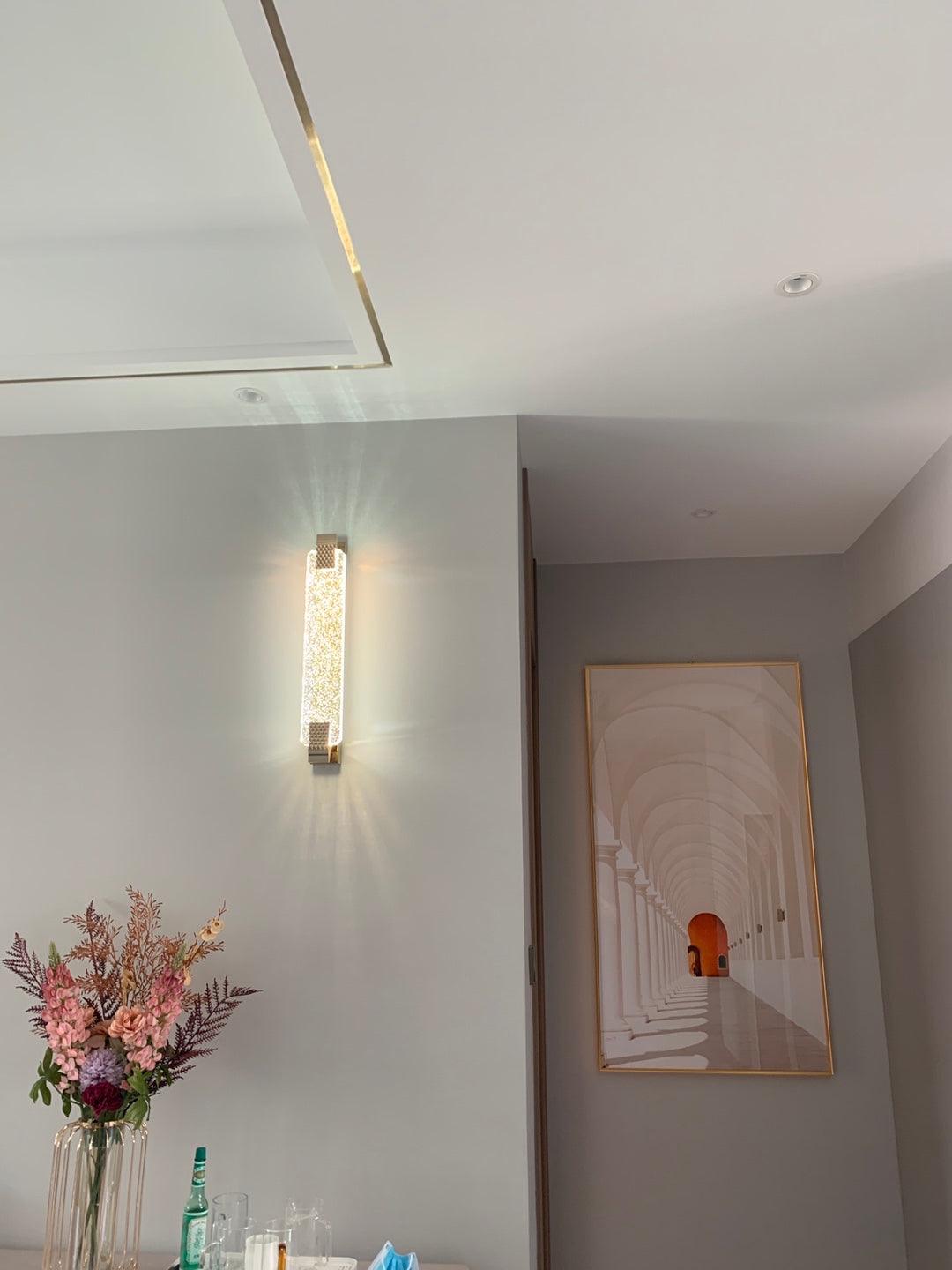 Wide room view of an illuminated Moet wall light above flowers, beside a corridor with a framed print