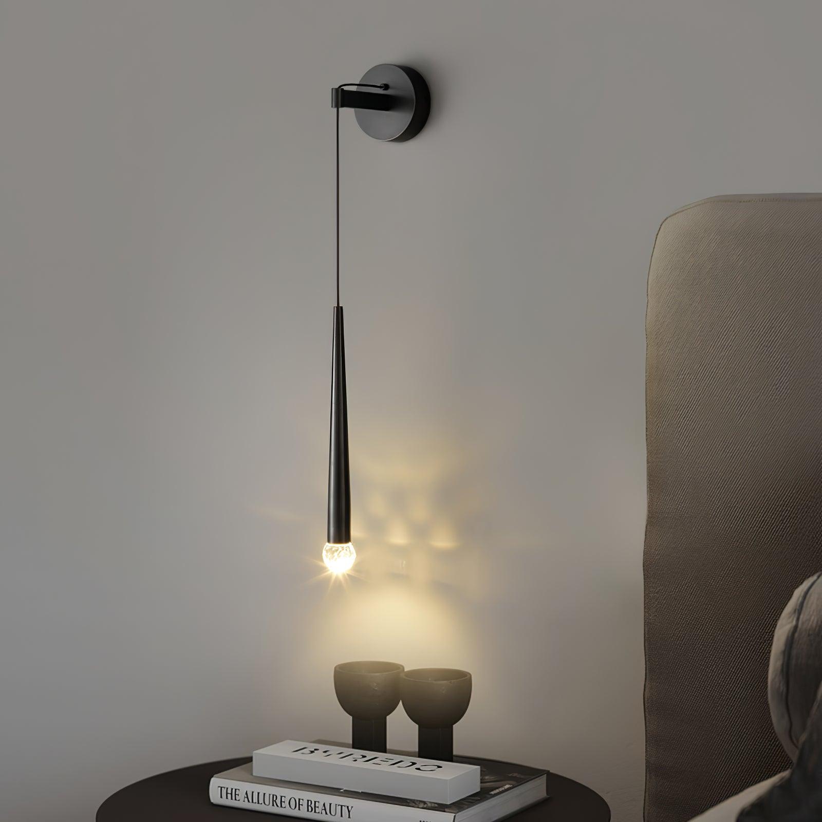 Lit black crystal-tipped wall light beside an upholstered headboard above books and two goblet ornaments
