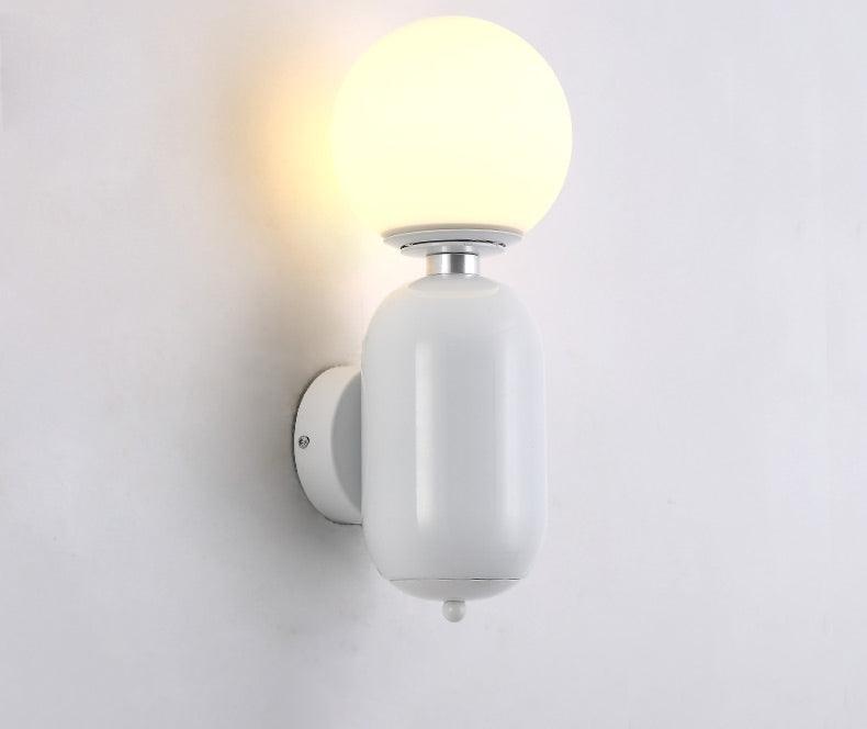 White Aballs sconce lit on pale wall, rounded white body and plate, silver-tone collar and small white lower finial