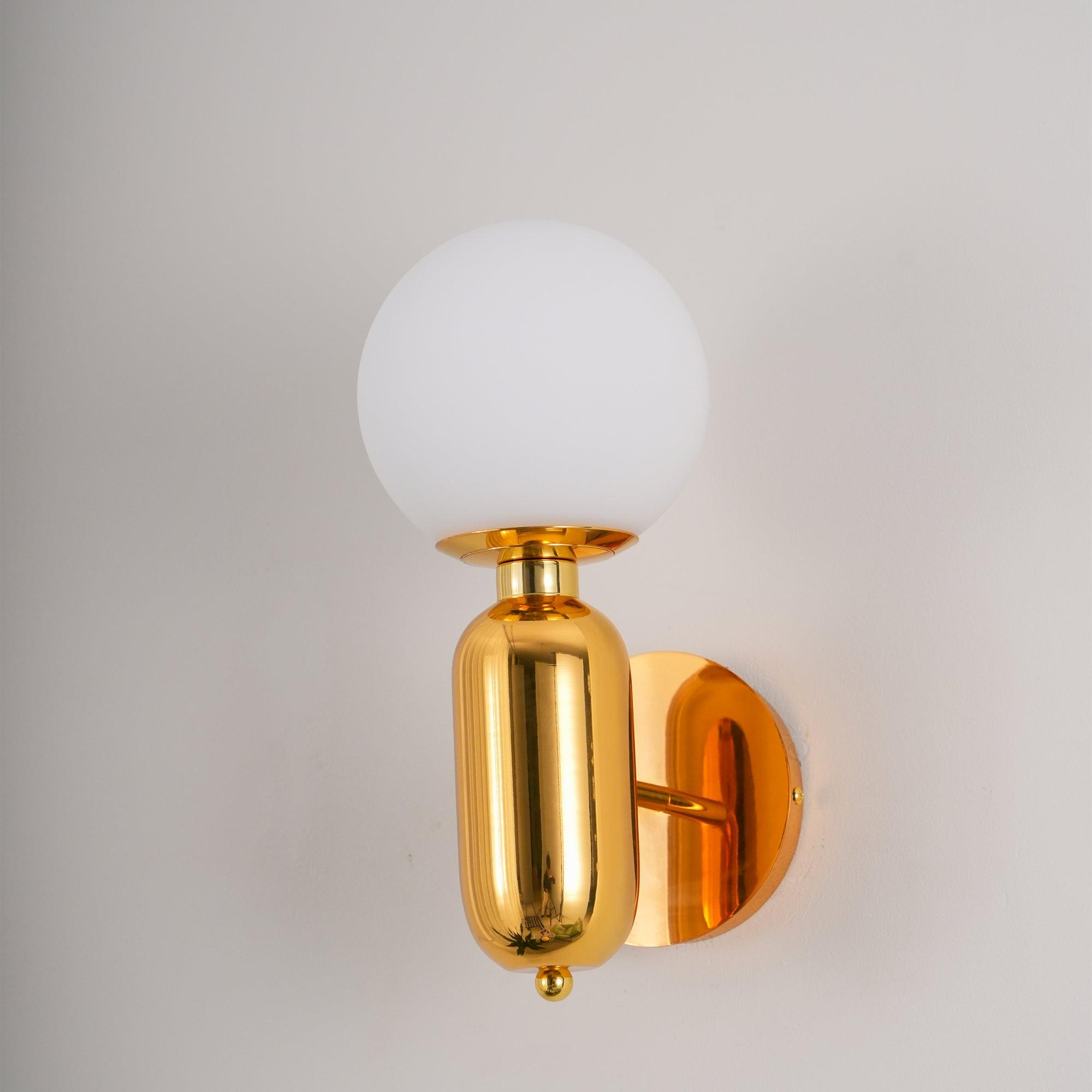 Angled gold-toned wall light with unlit-looking white globe, reflective capsule body, round plate and small finial
