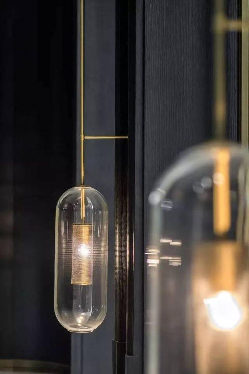 Gold-rod Vadim glass light on dark wall, with a second glass shade blurred in the foreground
