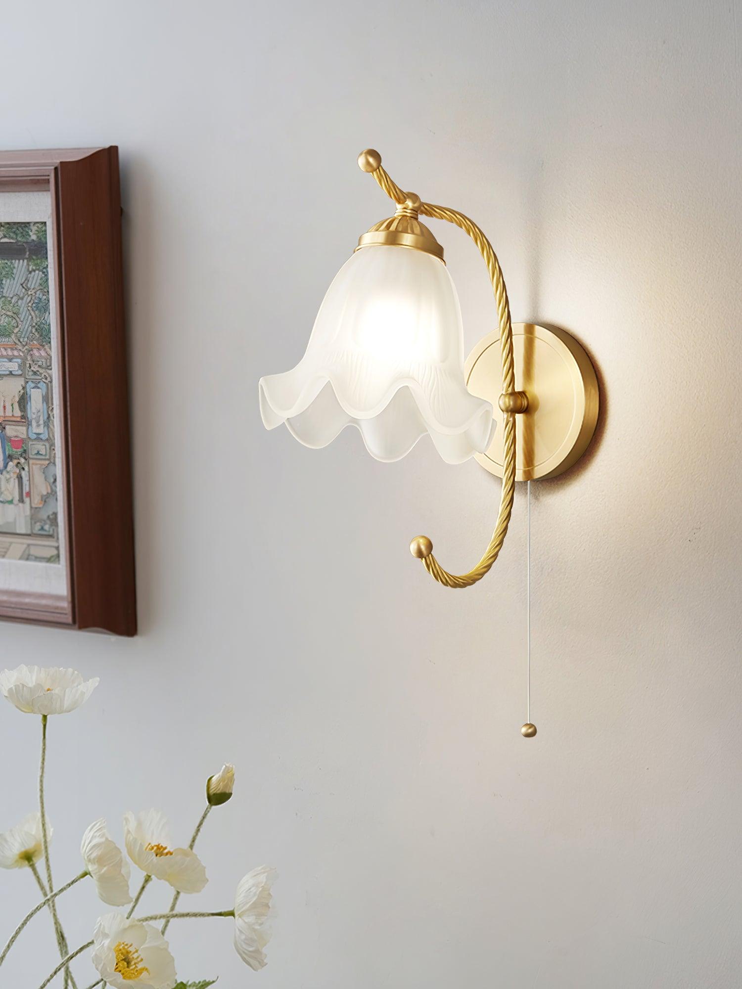 Close lit scalloped glass lamp beside framed artwork and white flowers, with twisted brass-finish arm and long thin pull cord