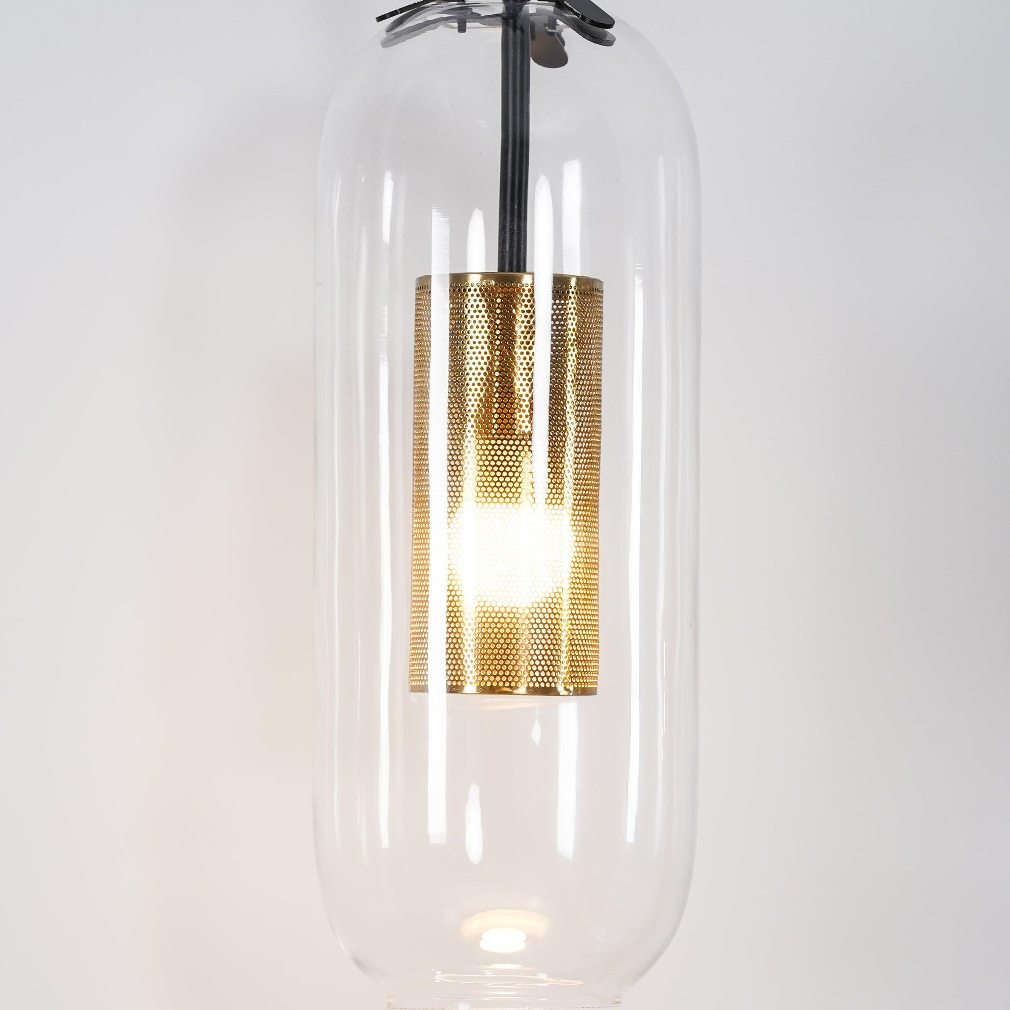 Close-up of clear Vadim glass shade around lit gold-coloured perforated cylinder, black rod and retaining clips