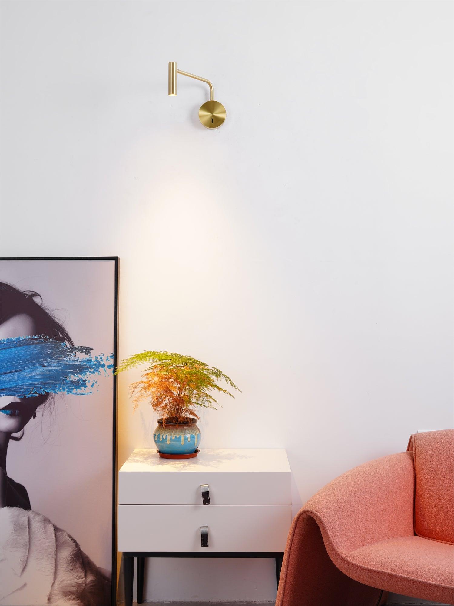 Gold-coloured wall light above a white side cabinet beside a coral armchair