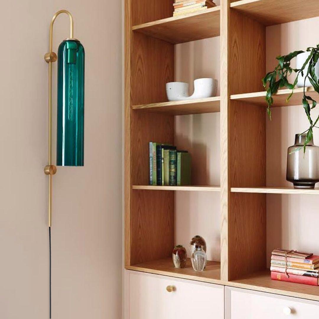 Dark teal tube wall lamp next to wooden shelving