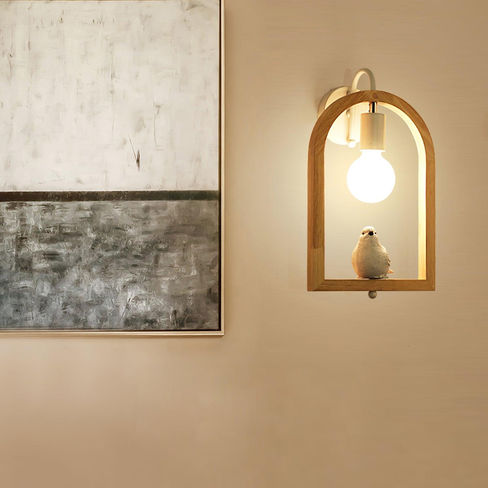 Lit bird wall lamp with a wooden arch and pale figurine beside a large monochrome framed painting