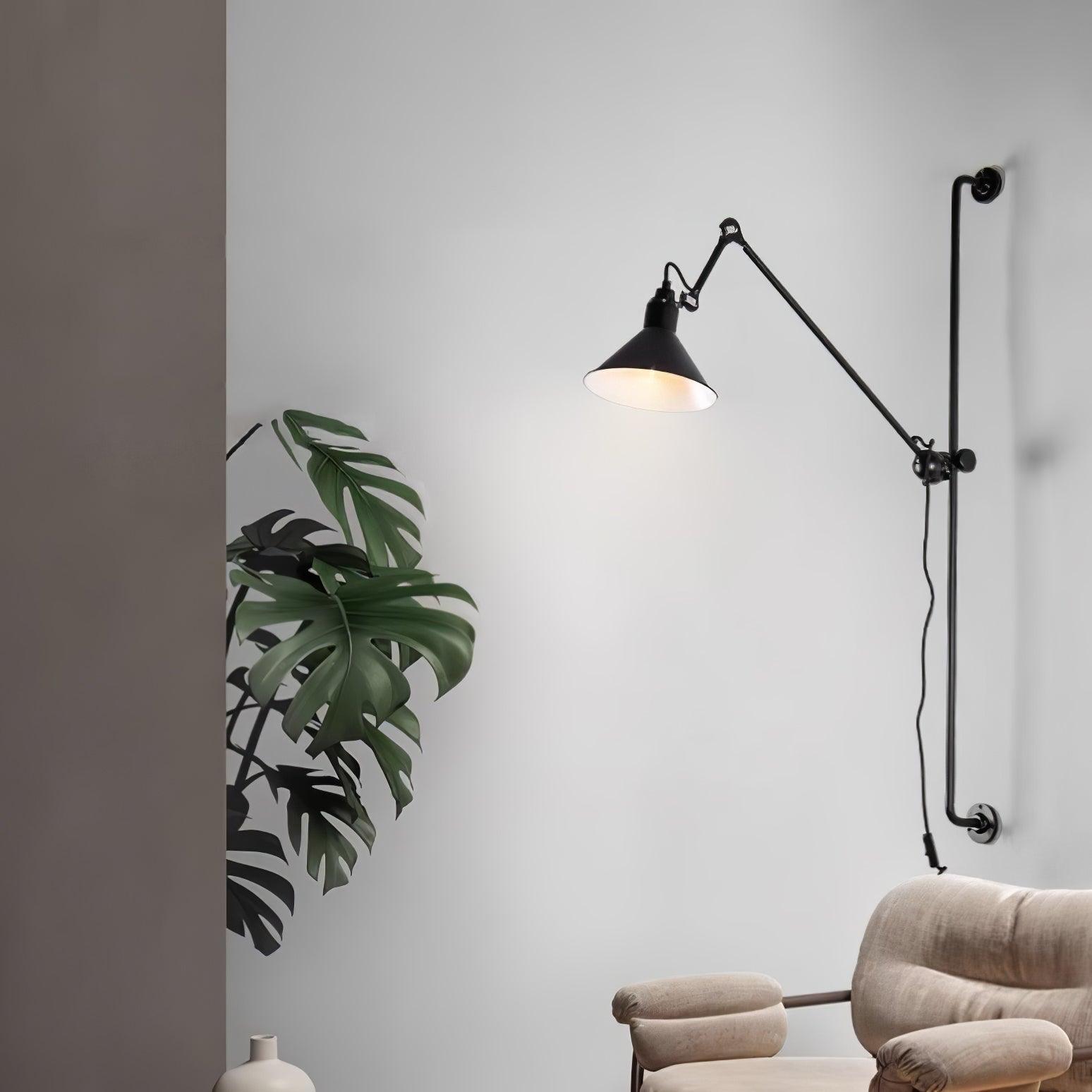 Black jointed wall lamp above a pale upholstered chair beside a leafy plant