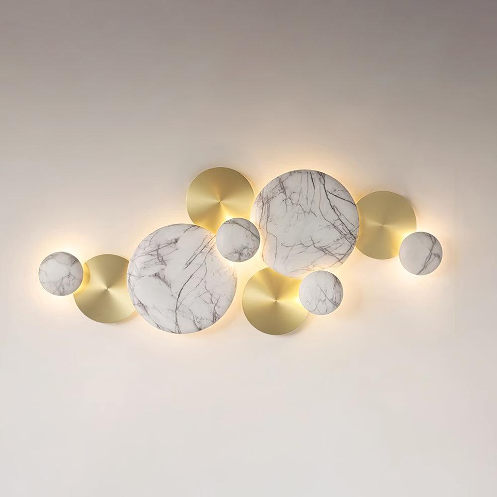 Front view of the lit marbled-pattern Pisco wall lamp, with white veined faces among gold-tone circles
