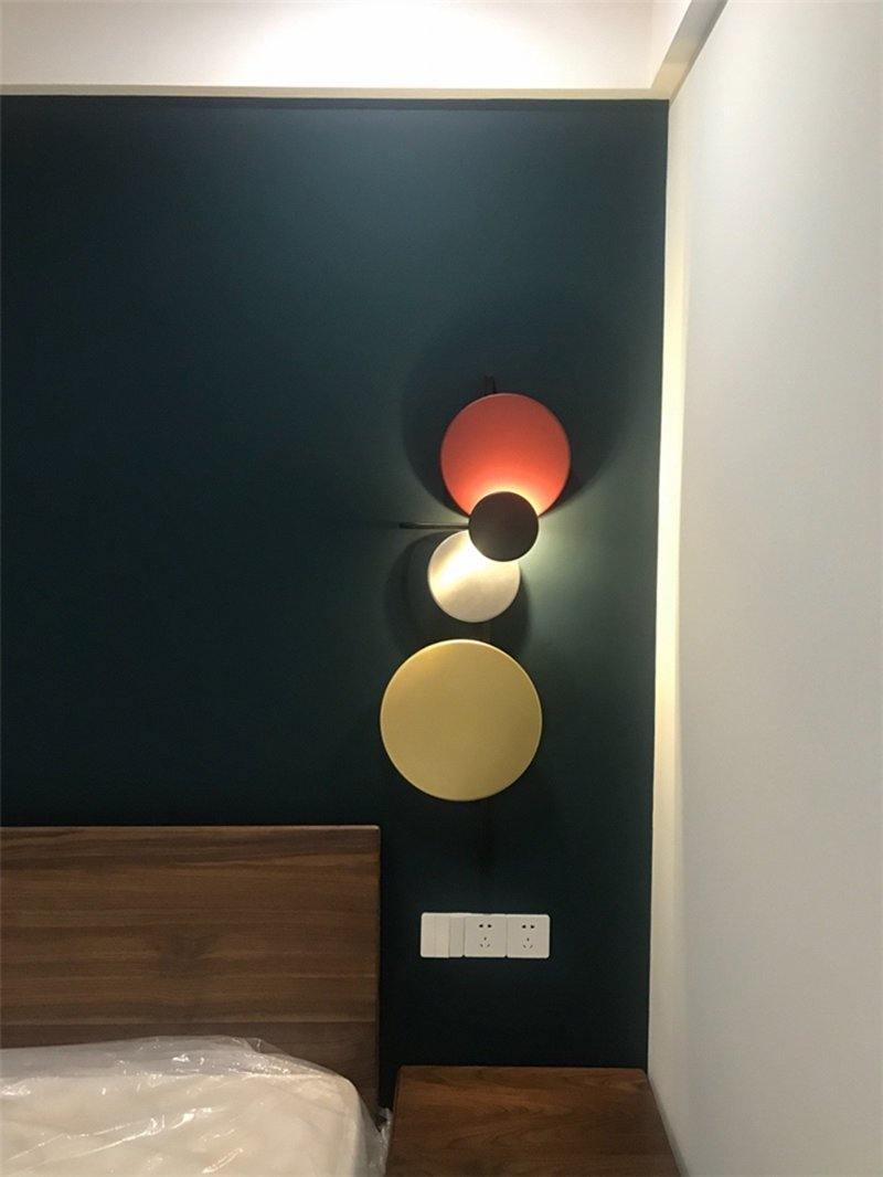 Red disc wall light above a wooden headboard against a dark wall