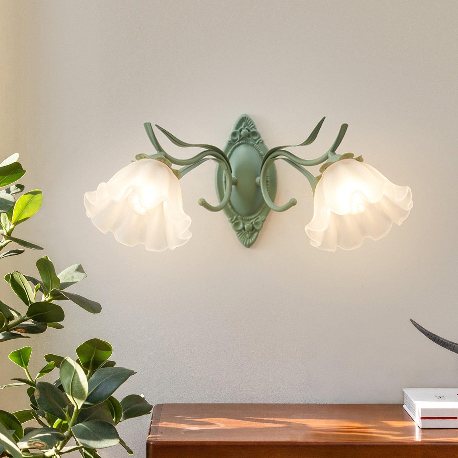 Green wall fixture with two glowing white flower shades above a wood console, with a plant and books nearby