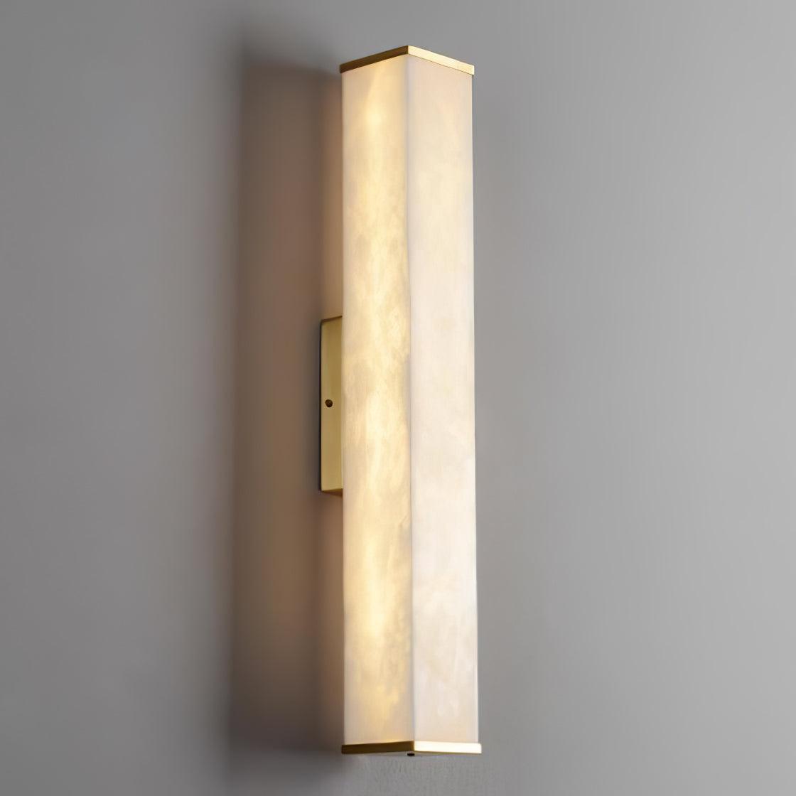 Three-quarter view of a lit alabaster cuboid on a gray wall, showing two veined faces and a brass mounting plate on the left