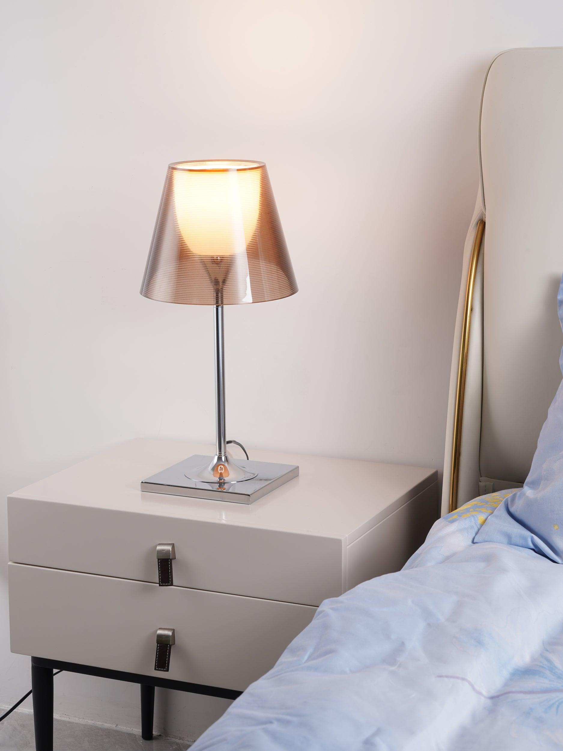 Illuminated Bronze Chrome Prism lamp beside a bed