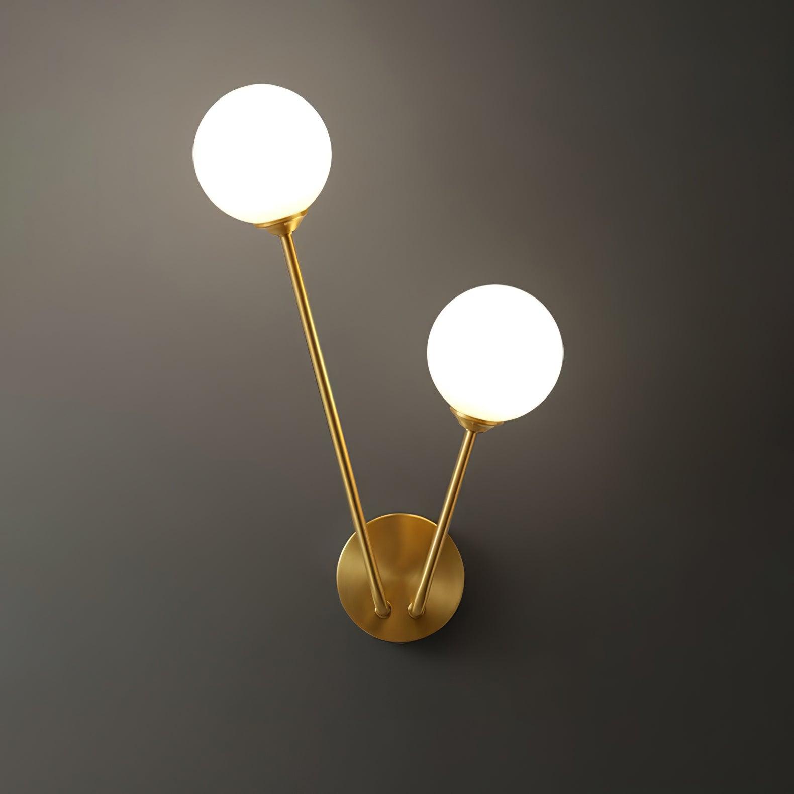 Front lit white globe wall light with uneven-height brass-tone stems and round wall plate