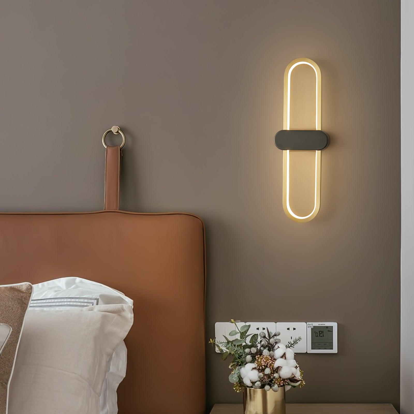 Closer view of the lit gold-loop wall lamp beside a tan bedhead and bedside flowers
