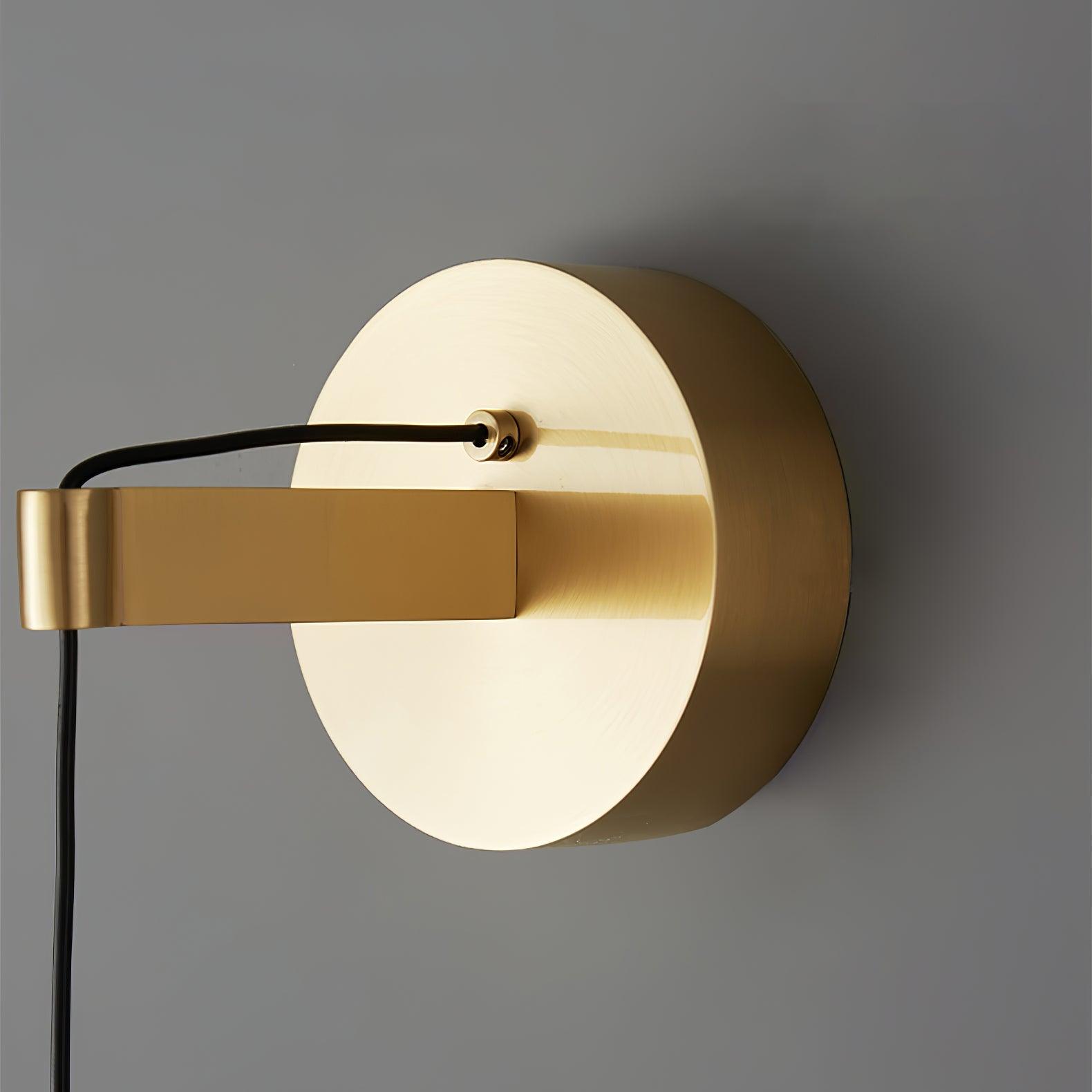Close-up of a round brass-tone wall plate, short rectangular arm and black cable entering the front cable gland