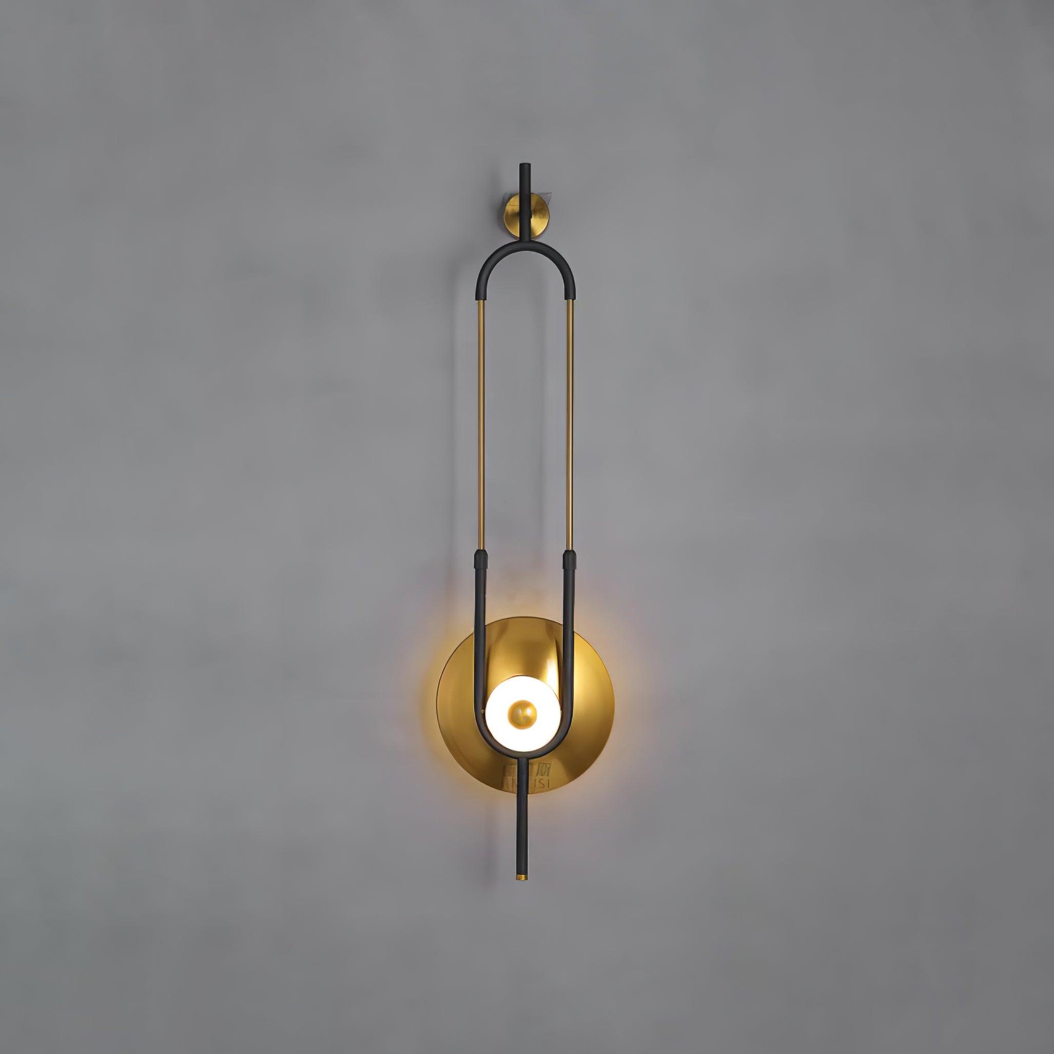 Frontal lit wall light on grey background showing black curved frame, gold rods and circular lower disc