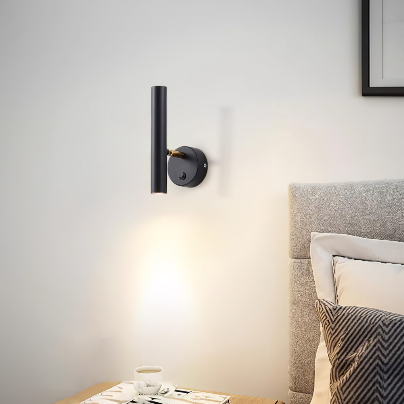 Upright black wall lamp beside a pale upholstered headboard, casting light down toward a cup and books