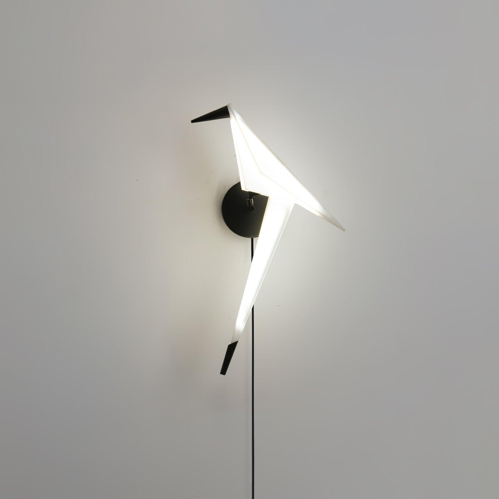 Alternate view of the glowing White bird wall light with Black beak, tail tip, round backplate and cable against a pale wall