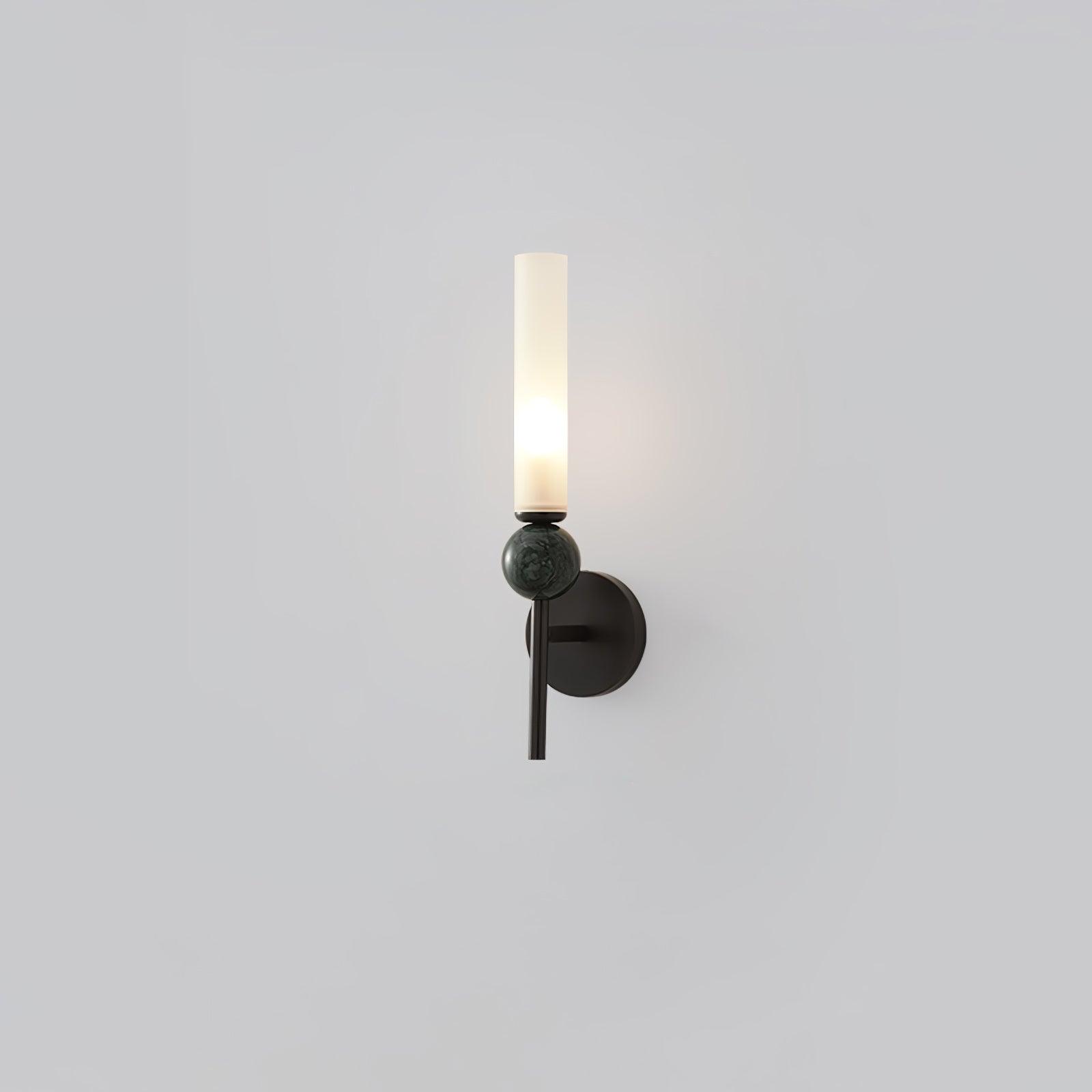 Straight black wall lamp with mottled green-grey marble sphere, round black plate and lit upright white cylinder