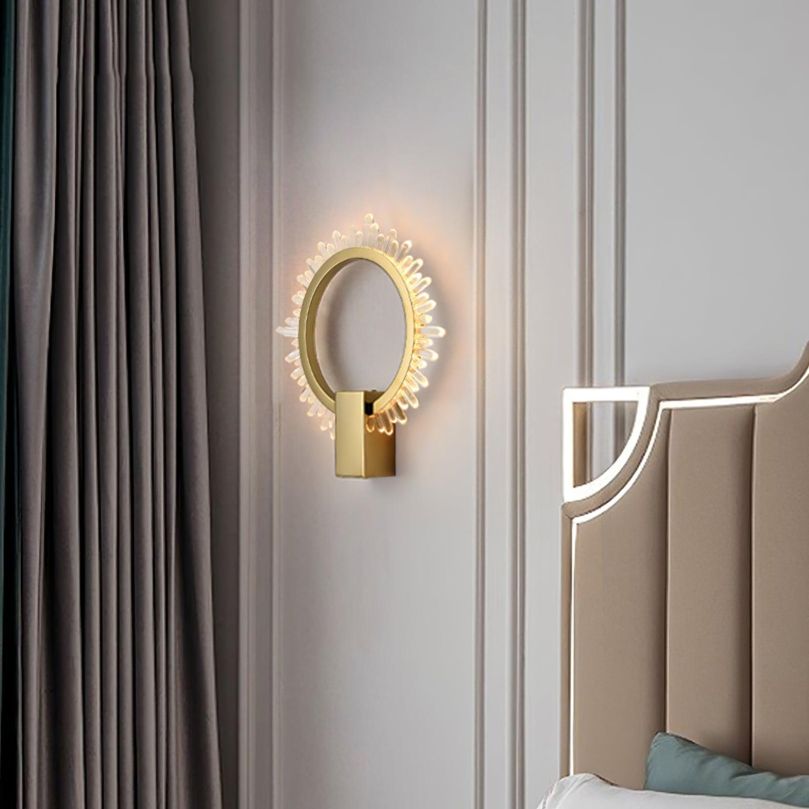 Crystal sunburst ring wall lamp beside a taupe upholstered bedhead and dark grey curtain