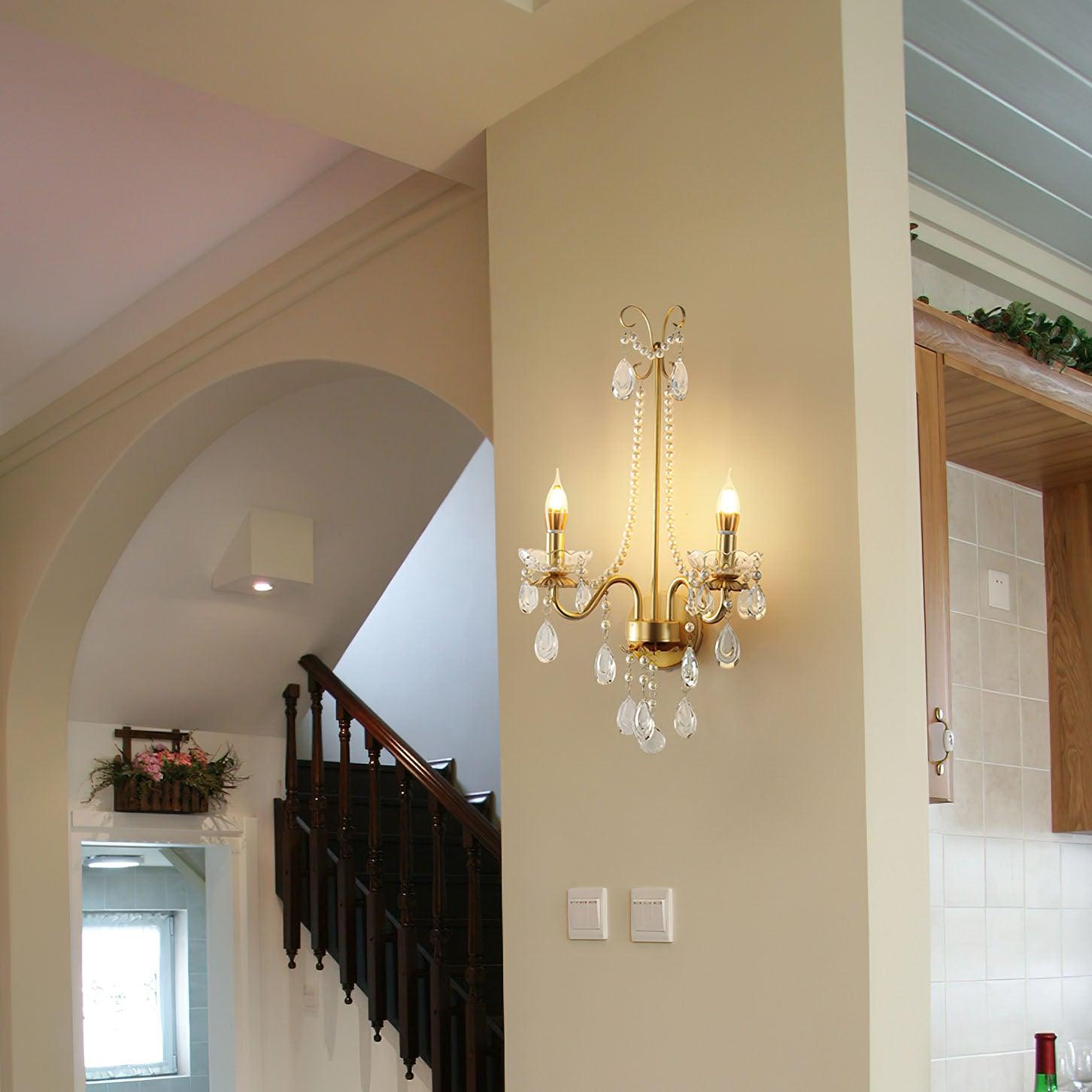 Lit wall fixture on pier beside arched staircase and dark wooden balustrade, with two wall switches below and tiled area at right