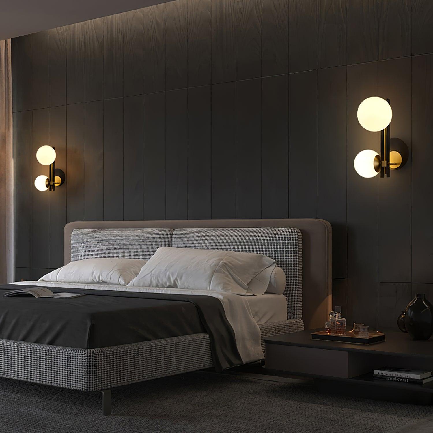 Two illuminated globe wall lights over a bed against dark wall panels, with a bedside table below