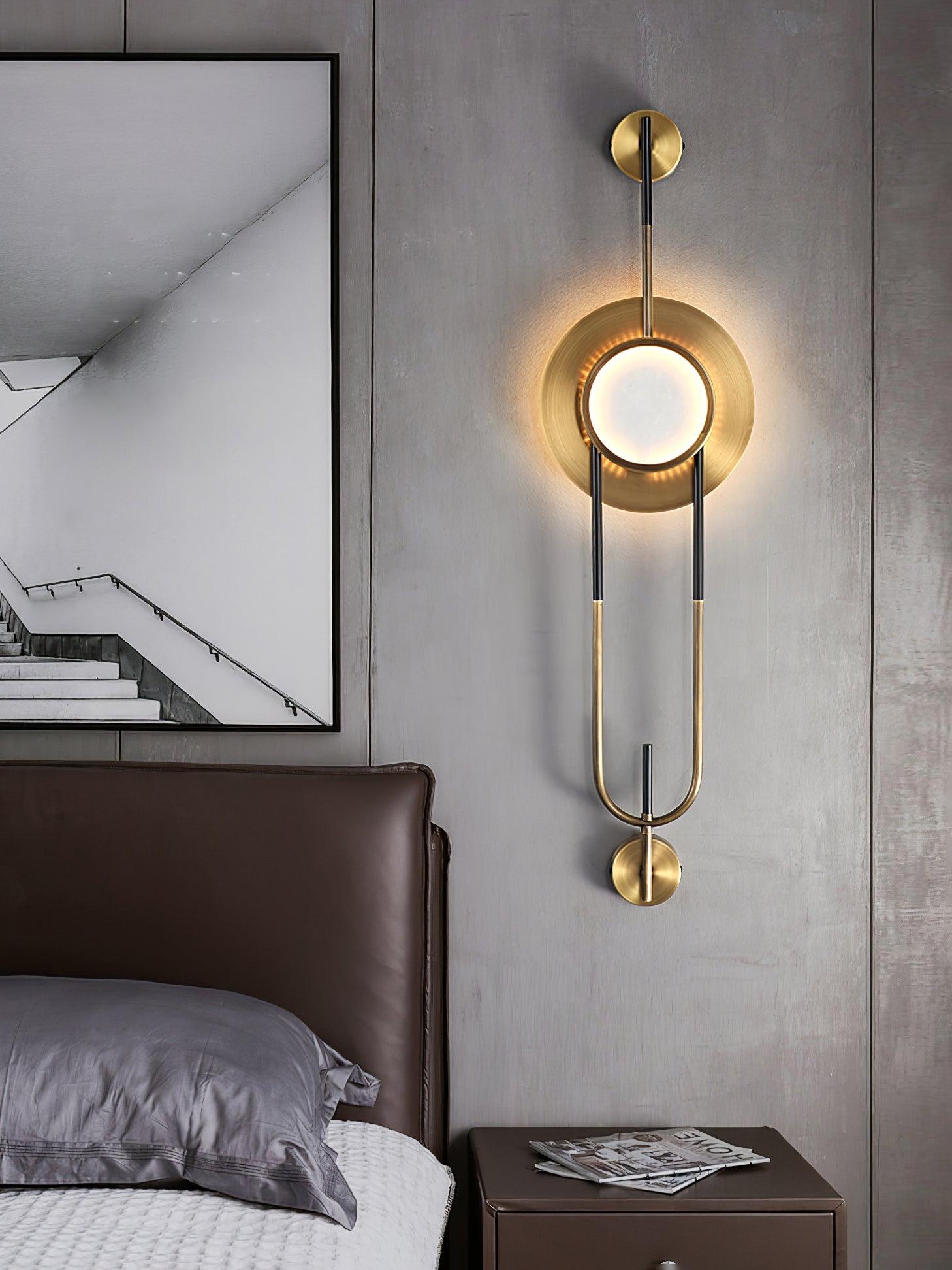 Bedside view of the circular LED wall light above a nightstand with magazines and gray pillows nearby