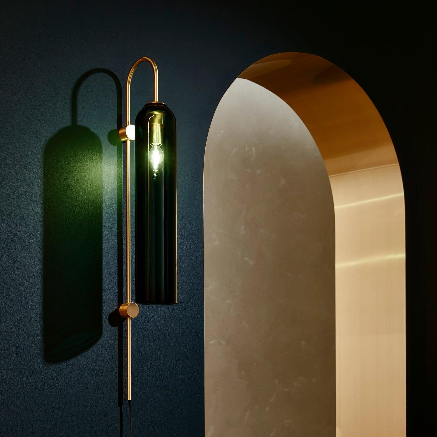 Tall dark glass wall lamp casting a strong curved shadow on a green wall