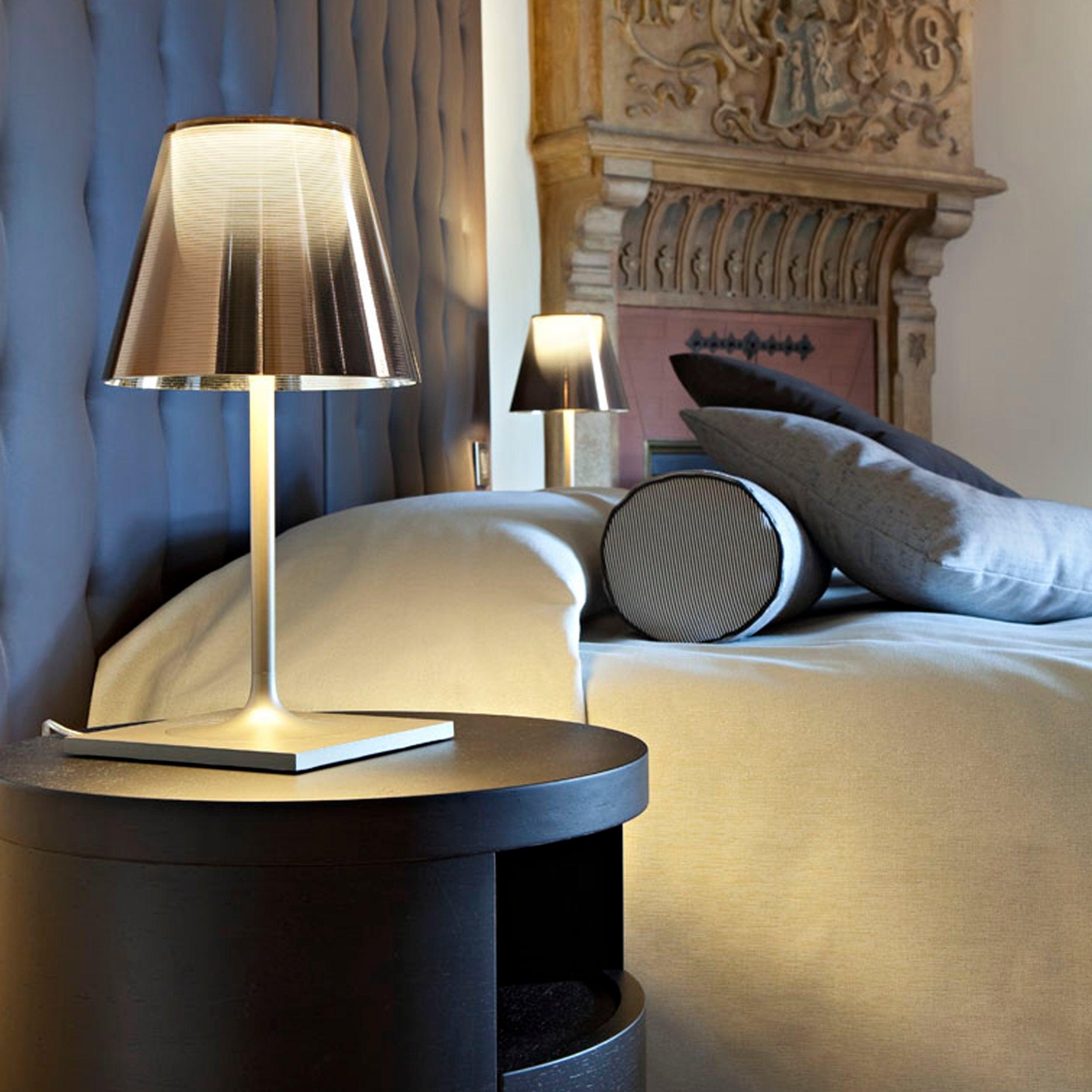 Chrome Prism table lamp beside an upholstered bed