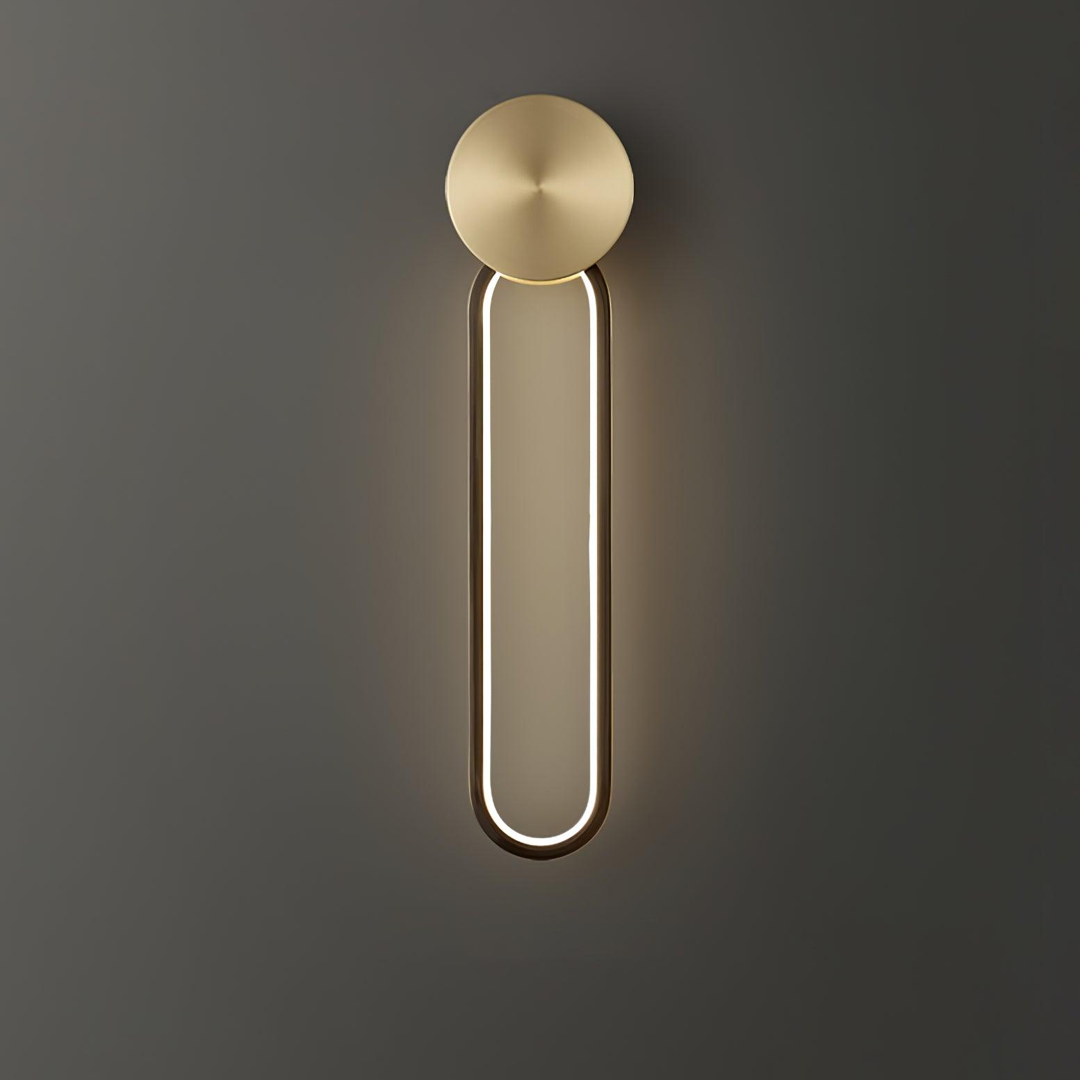 Illuminated black oval loop below a brass-tone circular disc, shown against a grey wall
