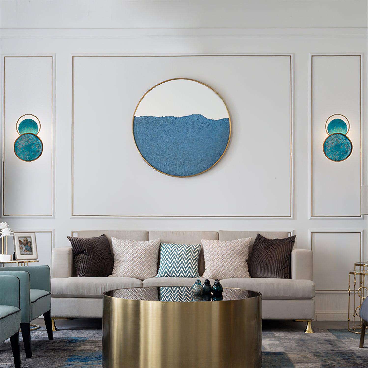 Two turquoise wall lights flanking a large circular wall decoration above a grey sofa and gold-coloured round coffee table.