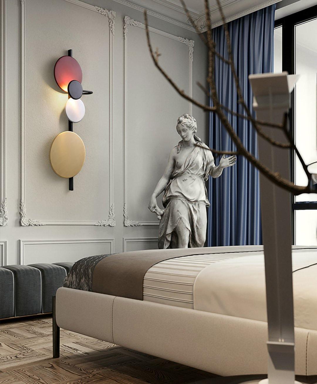 Vertical disc wall light on a panelled wall beside an upholstered bed