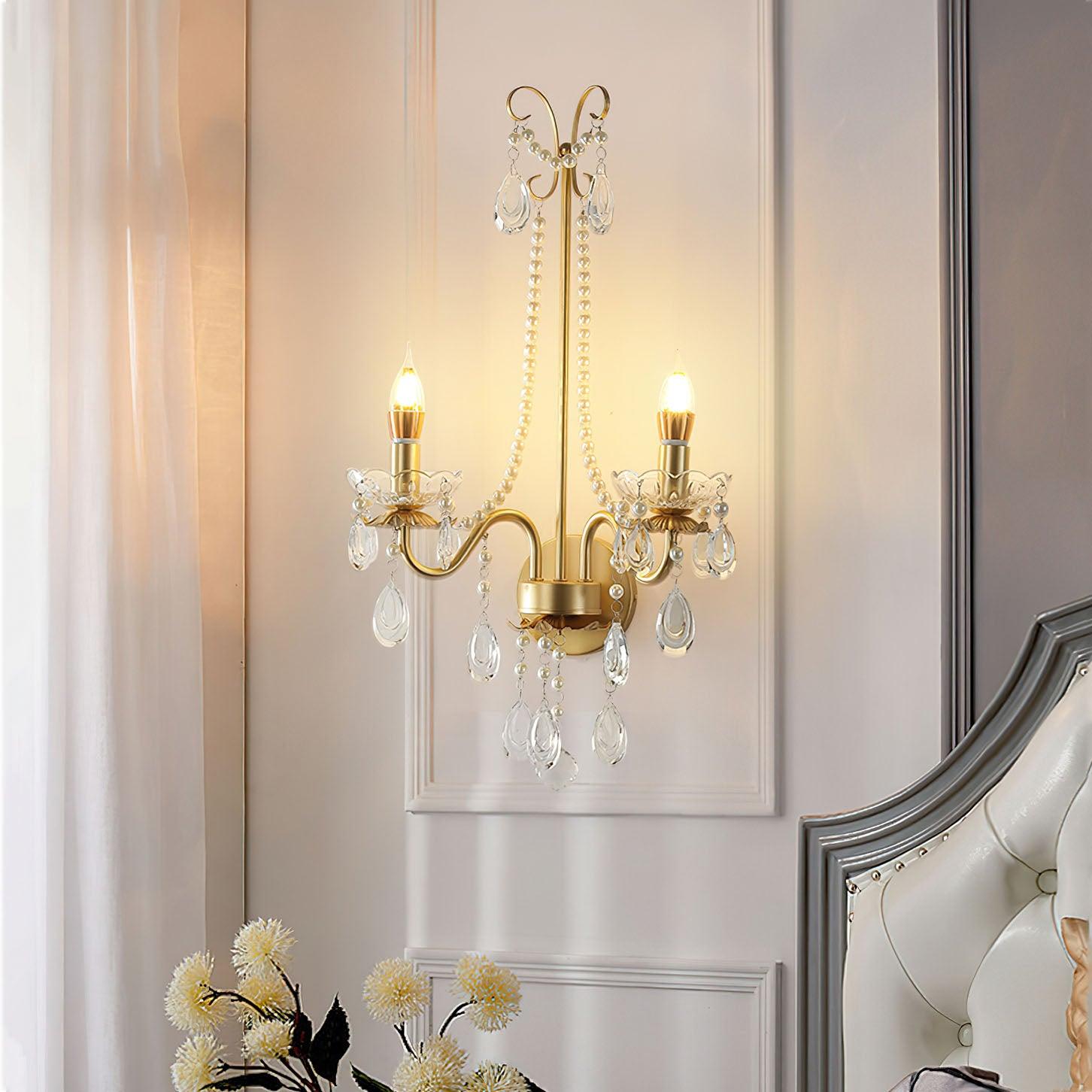 Lit bead-chain wall light beside white curtain and pale tufted headboard with silver frame, with flowers below