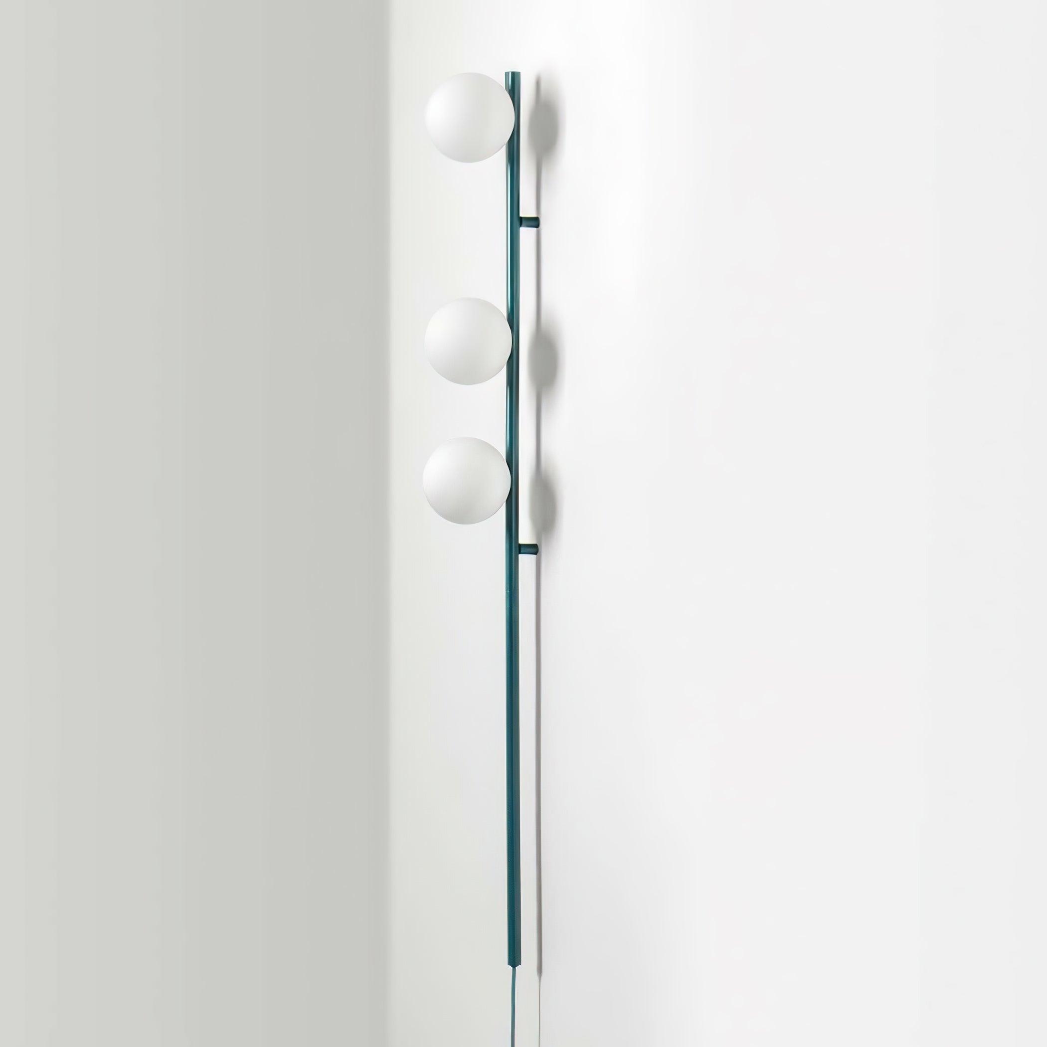 Side view of teal wall light, three white globes projecting from slim rod, two wall standoffs and shadows