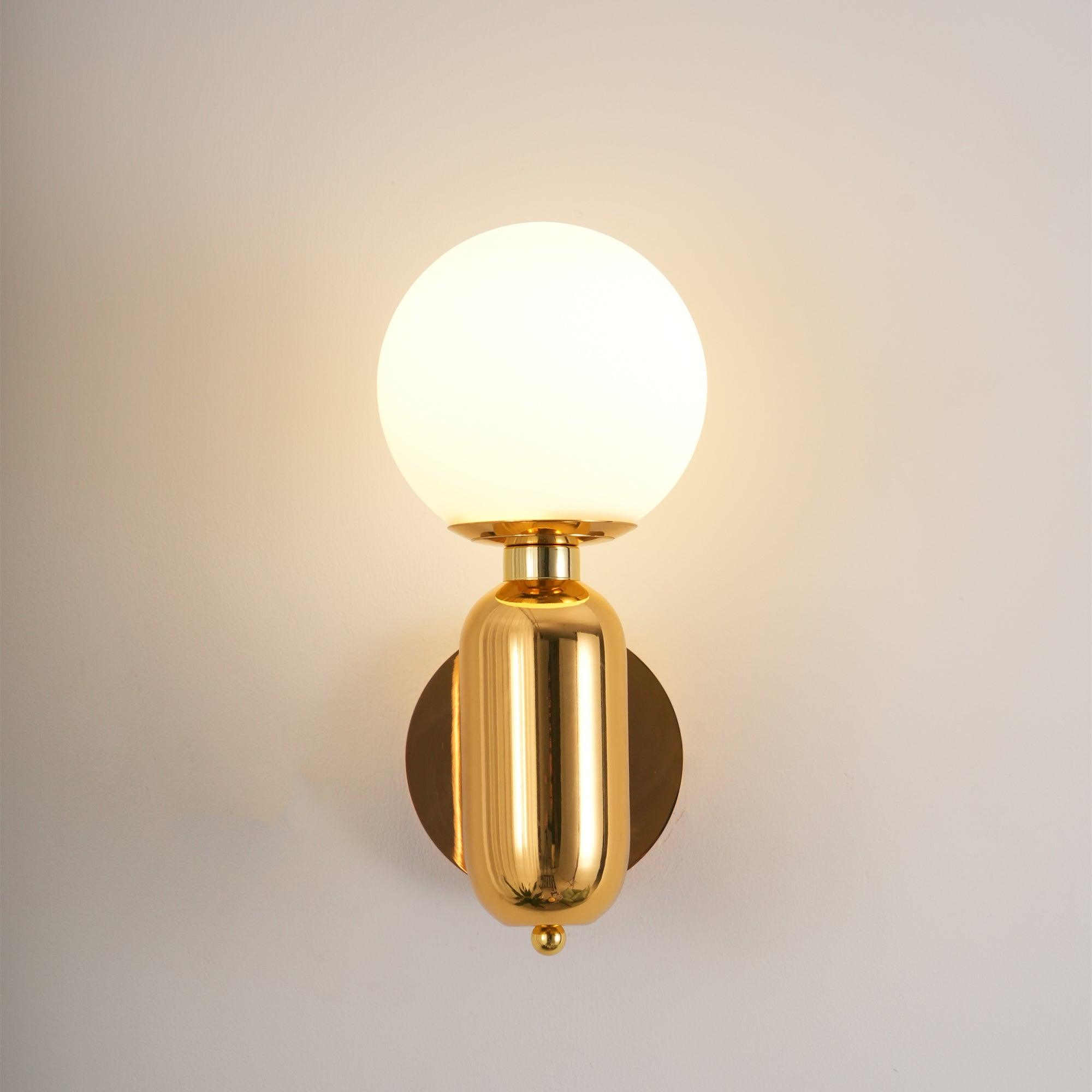 Gold-toned reflective Aballs wall light with lit white globe, rounded body, matching round plate and small lower finial