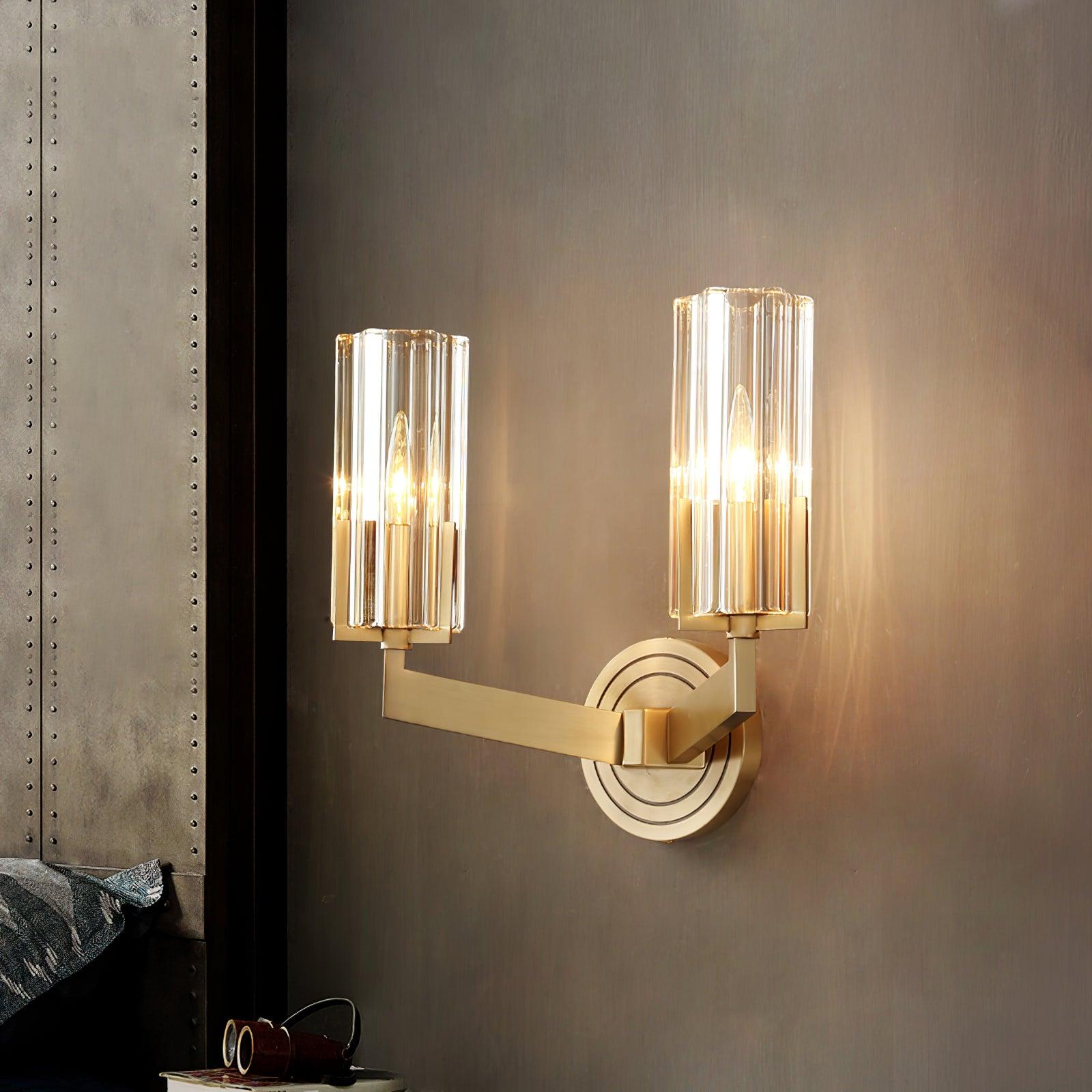 Close lit twin fluted glass shades on brass angular arms beside studded upholstered headboard, with binoculars and books below