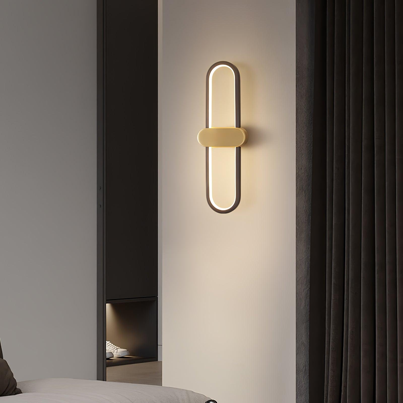 Black oval wall light with gold-coloured centre beside a tall wardrobe and dark curtain
