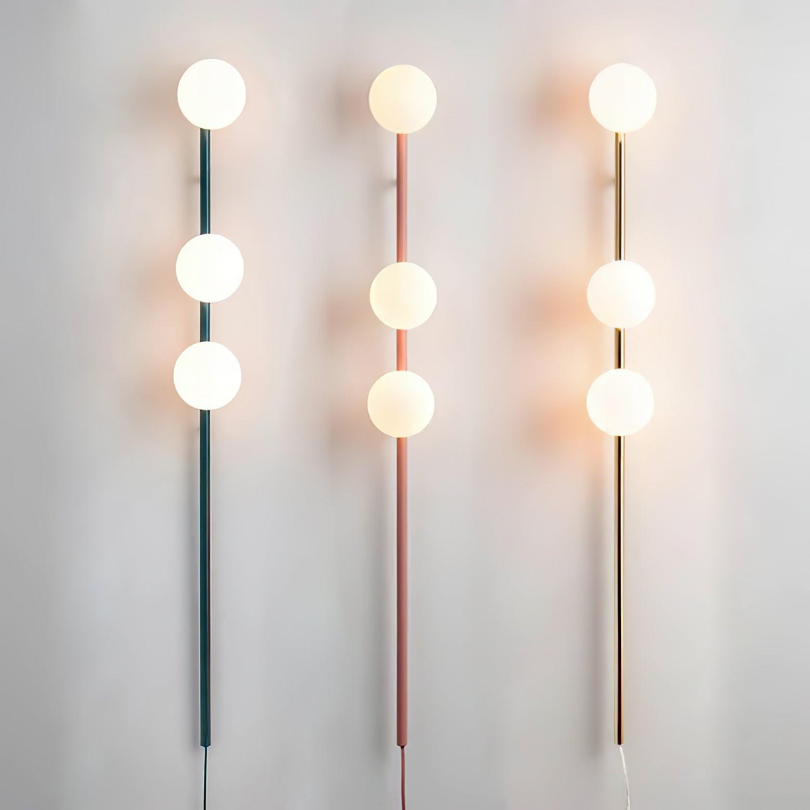 Three lit wall lights with teal, pink and gold stems, each carrying three white globes with lower cords visible