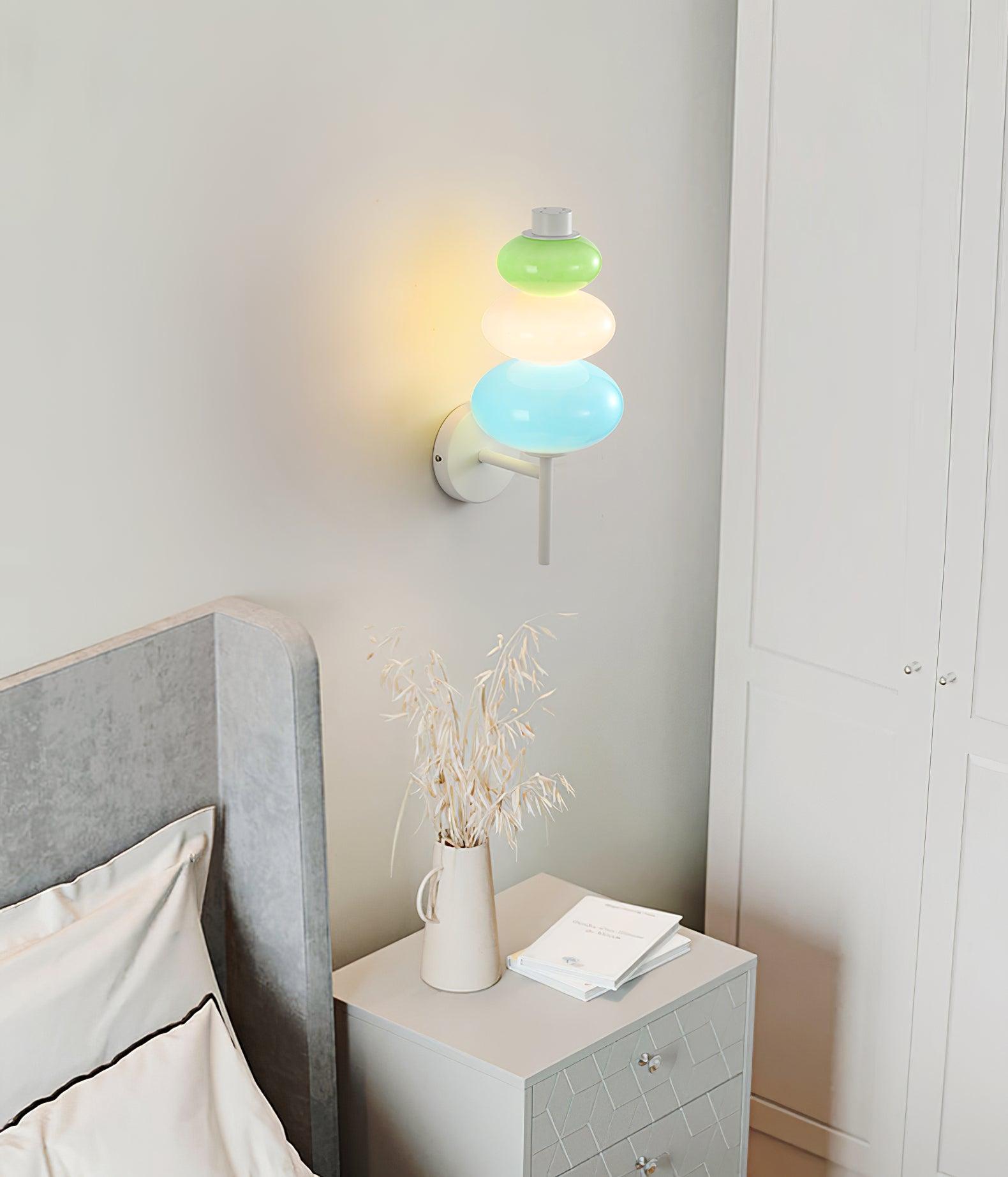 Lit glass wall lamp above a grey bedside cabinet with books and dried grasses near a grey headboard