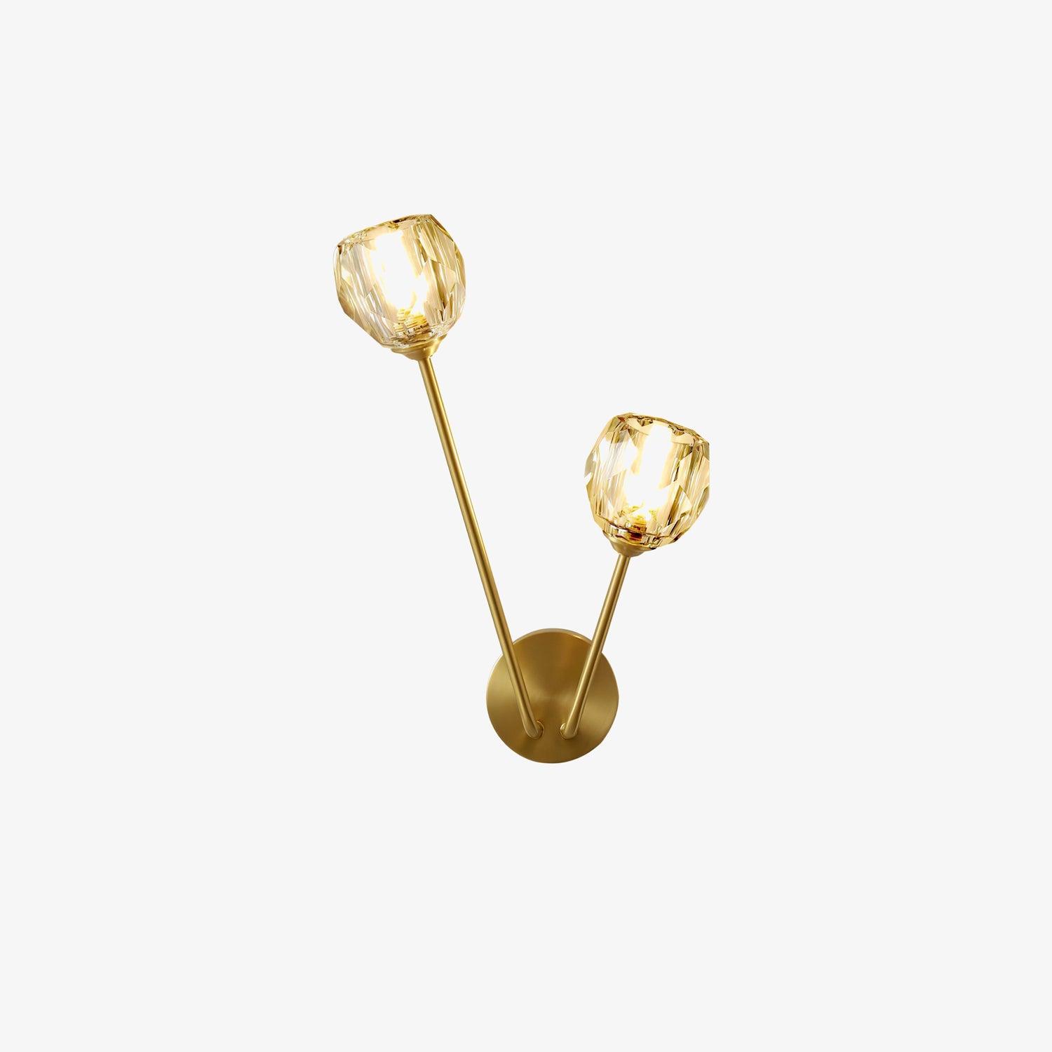 Isolated lit clear faceted wall light with two unequal stems and round brass-tone plate on white background