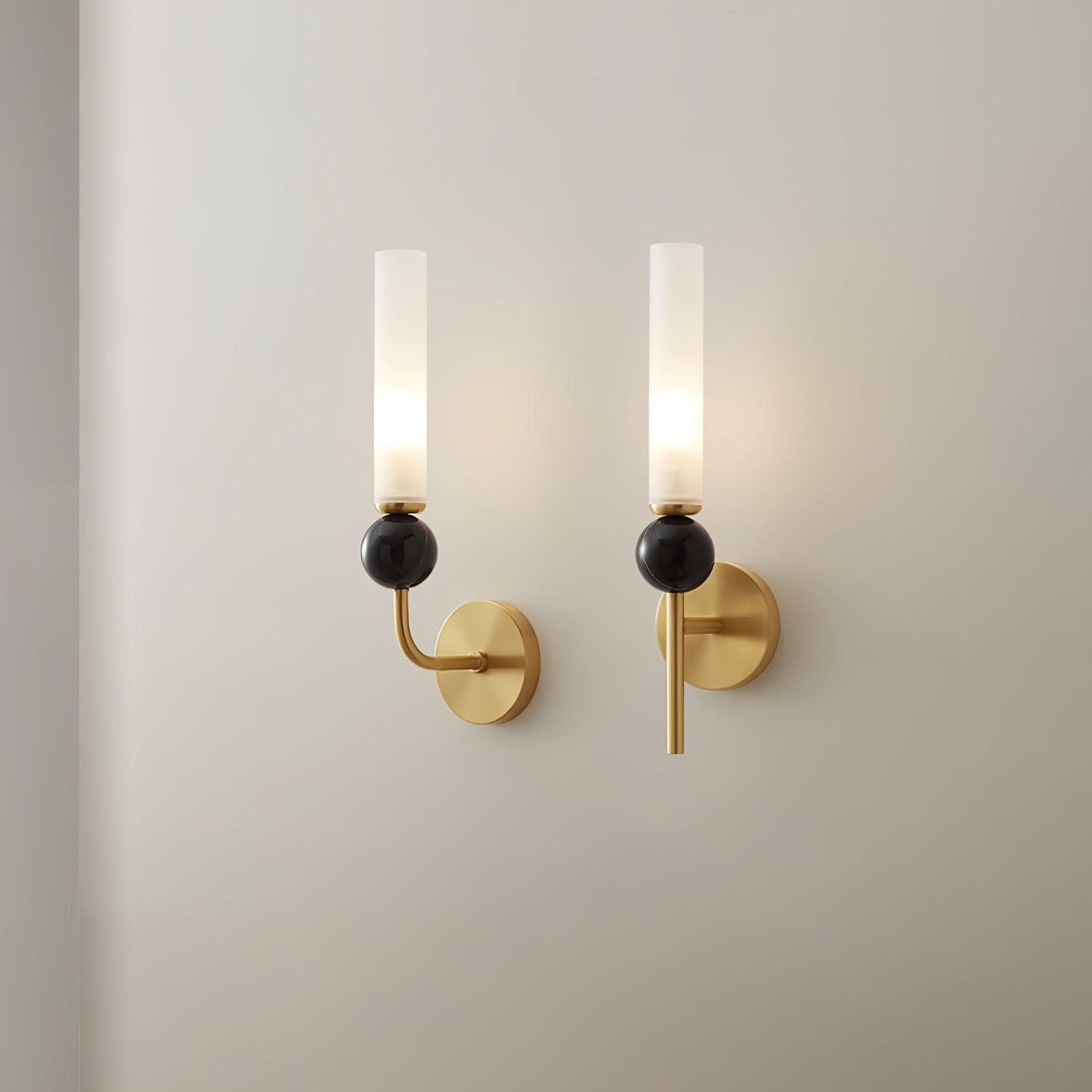 Curved-arm and straight-stem brass wall lights shown side by side, each with dark sphere, round wall plate and lit white cylinder