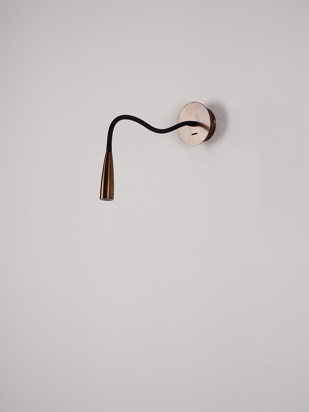 Oblique bronze reading light with sideways-curved black arm, downward head and USB opening in wall plate